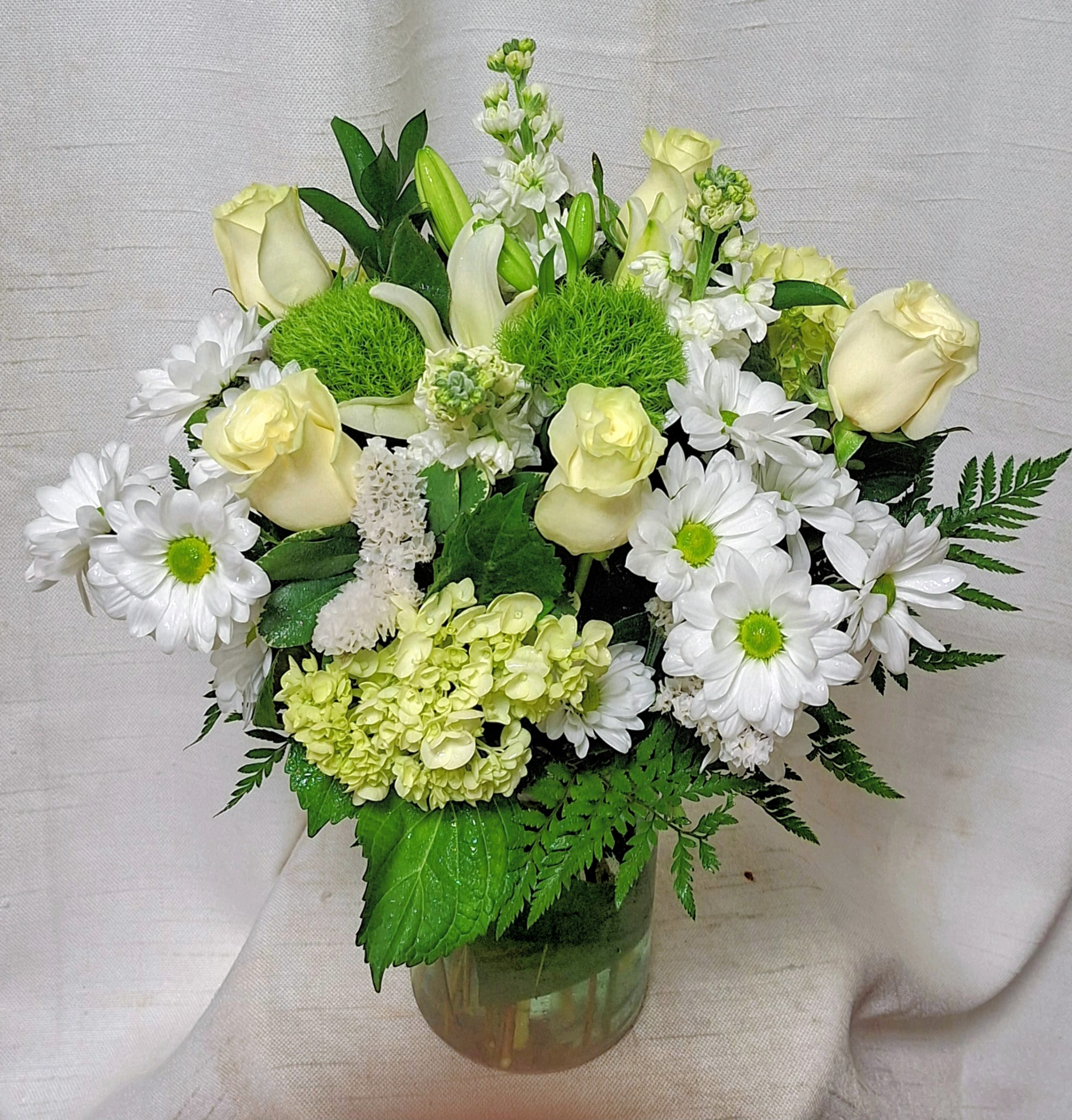 Reflective Affection (BR) - This exquisite arrangement features a delicate combination of white roses, green ball, green hydrangea, white stock, white lilies,  and white pom daisies, beautifully arranged with premium greens to create a serene and elegant atmosphere.  