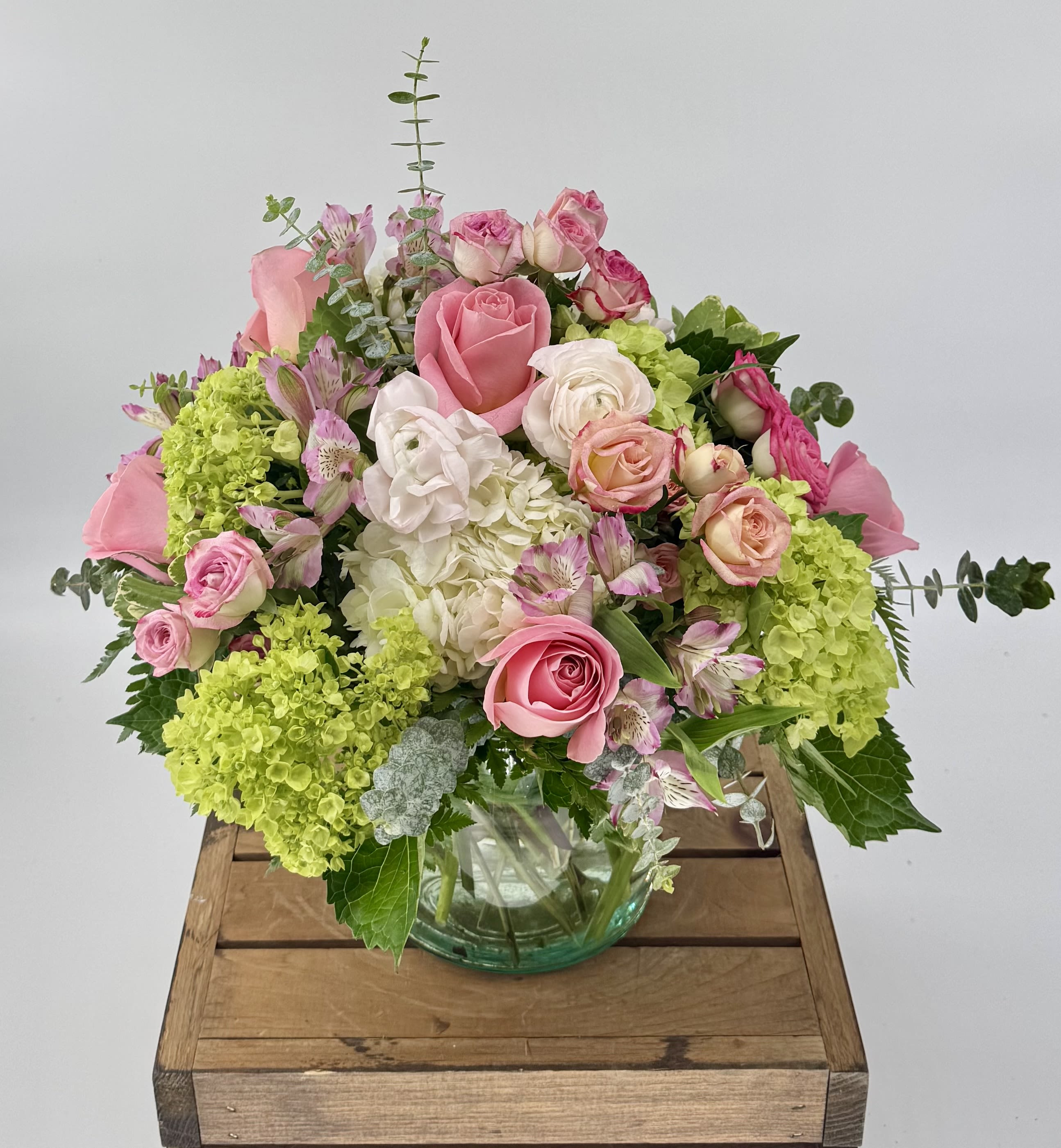 Simplicity (BR) - Delight in a stunning blend of green and white hydrangea, pink ranunculus, roses, alstroemeria, and eucalyptus, artfully arranged in a leaf-lined 6x6” clear vase—crafted to elevate your most cherished moments. 