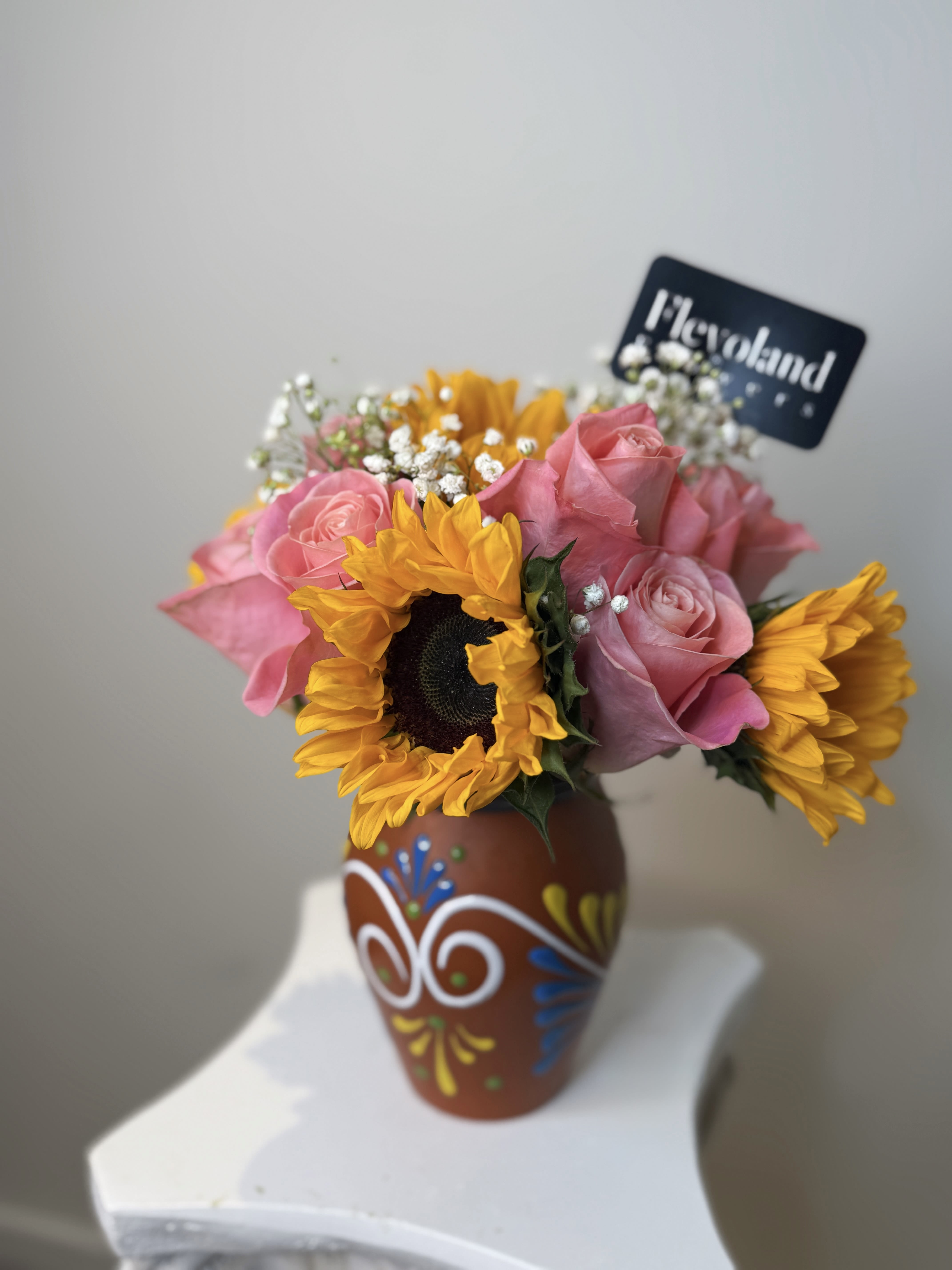 Soul of Mexico - A vibrant arrangement of sunflowers, pink roses and baby’s breath, presented in a hand-painted Mexican clay vase. Each piece is crafted in Mexico, bringing authenticity, culture and artistry to your floral gift.  A bouquet that celebrates tradition and beauty, perfect for brightening spaces with color and heritage. 