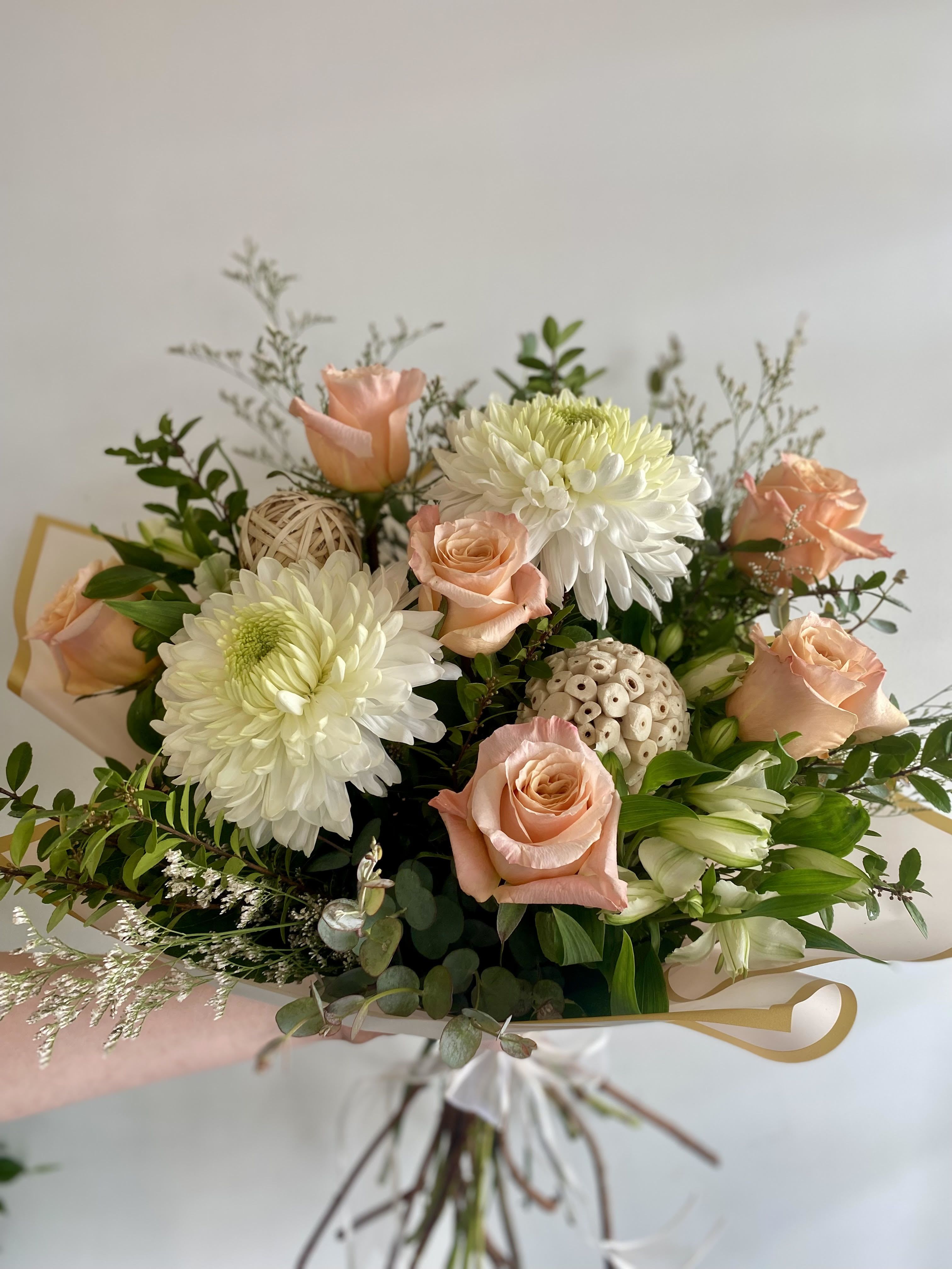 Hand-Tied Bouquet #15 Hand-Tied Bouquet #15 - A soft and sophisticated bouquet showcasing creamy white chrysanthemums, delicate peach roses, and white alstroemeria. Accented with eucalyptus, airy fillers, and unique natural elements like lotus pods and rattan spheres, this arrangement blends elegance with a touch of rustic charm—perfect for serene celebrations or thoughtful gestures.