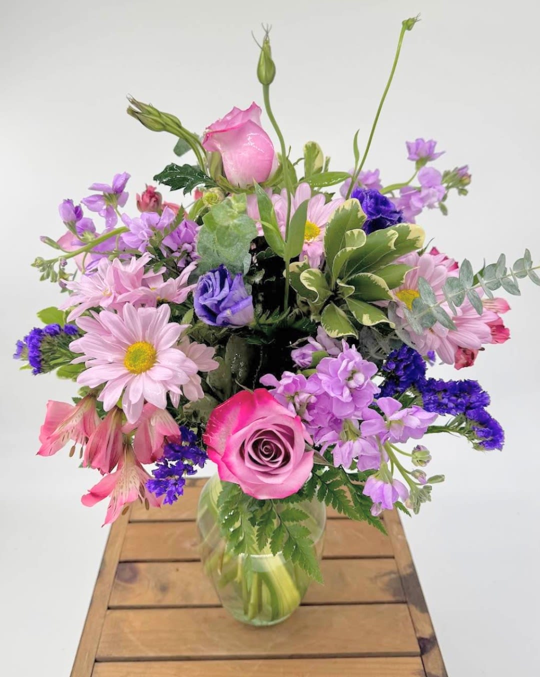 Breezy Lavender (BR) - Introducing &quot;Breezy Lavender&quot;, a breathtakingly beautiful flower arrangement that is sure to bring tranquility and calmness to your space. This stunning bouquet is composed of delicate lavender and white roses, accompanied by purple stock, purple alstroemeria, and expertly arranged with greens and filler in a clear glass vase. 