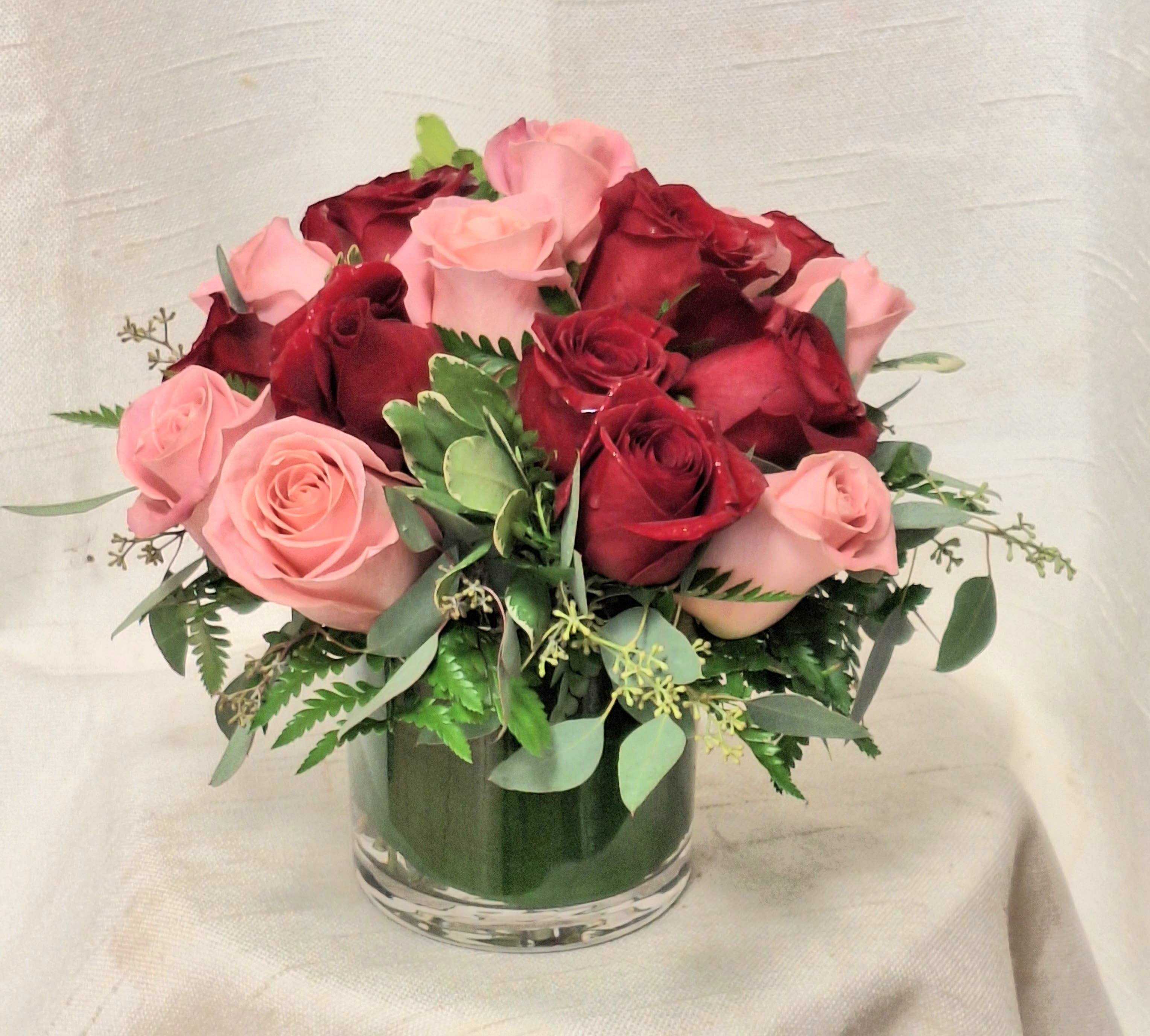 Sparks (BR) - Embrace modern elegance with our exquisite floral arrangement featuring a striking combination of red and pink roses, skillfully arranged in a leaf-lined glass vase and complemented with assorted greenery. This deluxe presentation exudes sophistication and charm, making it an ideal choice for adding a touch of contemporary beauty to any occasion or space. Elevate your decor with this captivating arrangement.  As Shown in Deluxe ( 18 Roses )