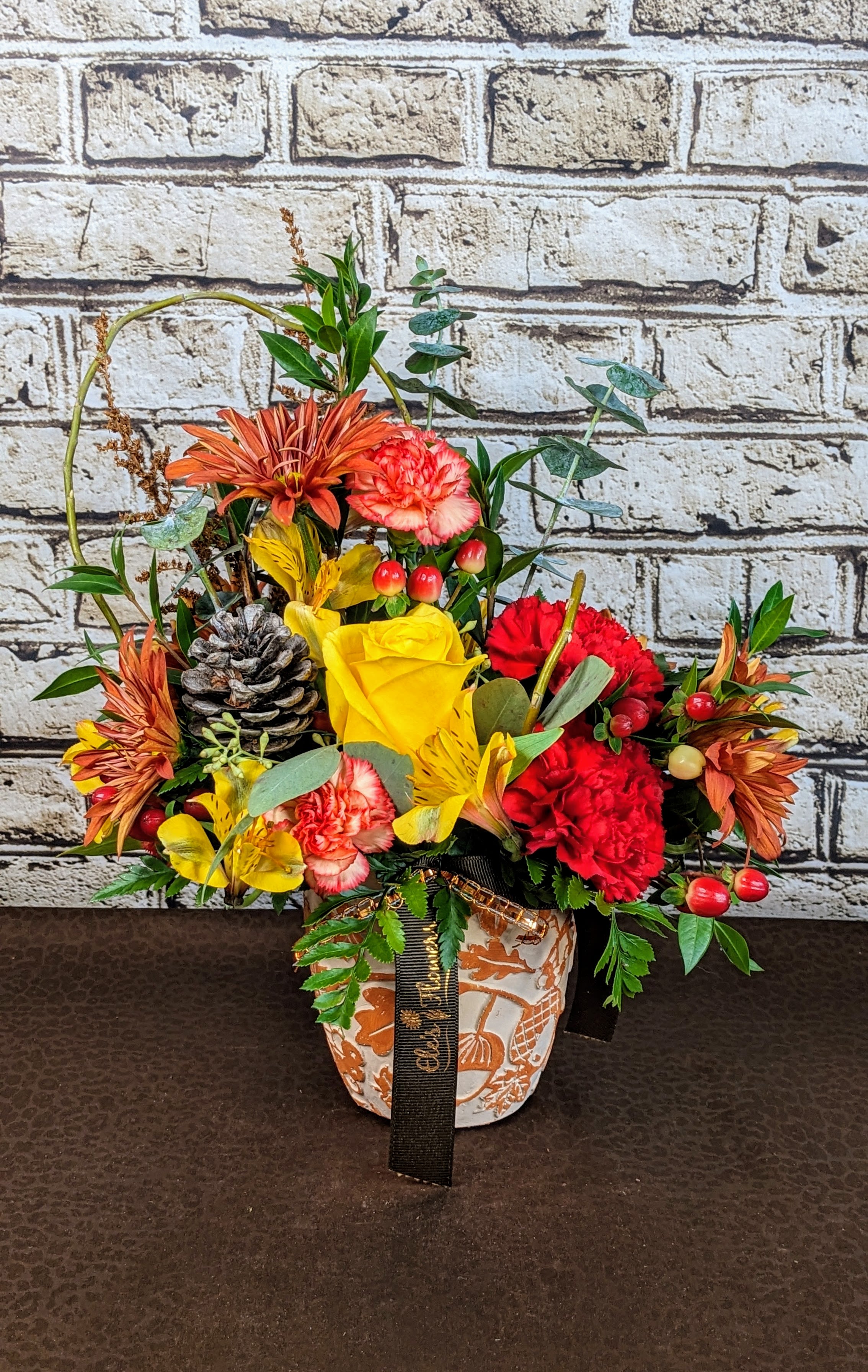 Autumn Vibes - Autumn Vibes is a petite fall arrangement thoughtfully designed in a charming ceramic pot with autumn-inspired patterns &amp; tones making it the perfect small centerpiece. Featuring a harmonious mix of warm yellows, rich reds, and vibrant oranges, it captures the essence of the season in a compact form. Textured greenery and subtle natural accents like berries or dried foliage add depth and character. Perfectly sized for intimate gatherings or cozy spaces, this arrangement brings a touch of seasonal warmth and charm to any table or corner.   Blooms and container may vary from photo.   The designs we create are custom and the blooms and containers will vary. We use the freshest product available to create the perfect floral combination for the recipient. If you have any special requests, please add those in the &quot;special instructions&quot; portion of your order to help us dial in your vision. Otherwise, our skilled designers, Sara &amp; Brett, will take it from here!  Approximate Dimensions: 14&quot;H x 11&quot;W