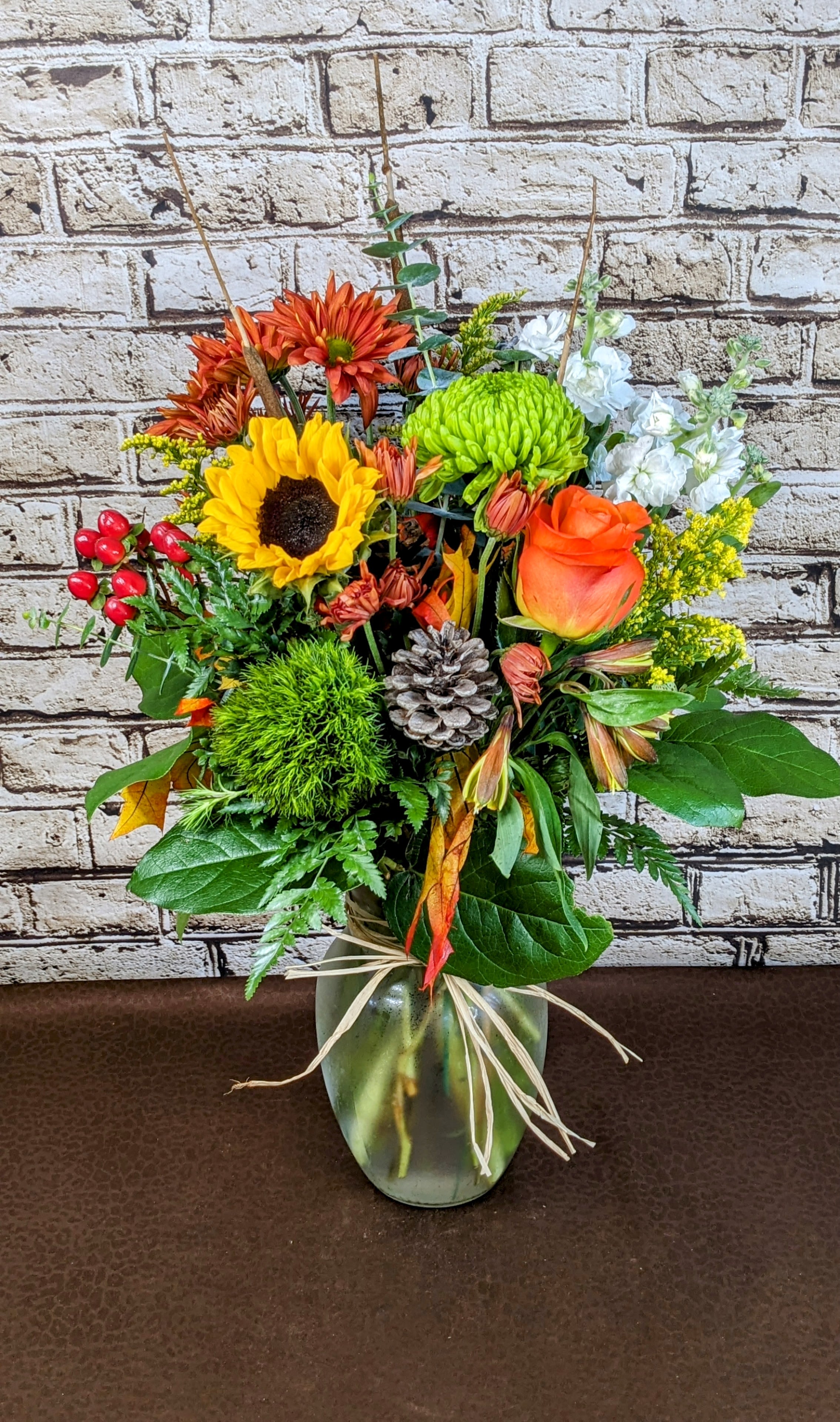 Fall Cheer - This cheerful fall arrangement bursts with the vibrant hues of the season, featuring warm yellows, sunny oranges, and lush greens, beautifully balanced with crisp pops of white. The white accents brighten the composition, adding a fresh, uplifting touch to the traditional autumn palette. Textured greenery enhances the arrangement’s fullness, while seasonal elements like berries add a natural vibe. Arranged in a classic vessel, this design brings a joyful and inviting energy to any fall celebration or space.  Blooms may vary from photo.   The designs we create are custom and the blooms and containers will vary. We use the freshest product available to create the perfect floral combination for the recipient. If you have any special requests, please add those in the &quot;special instructions&quot; portion of your order to help us dial in your vision. Otherwise, our skilled designers, Sara &amp; Brett, will take it from here.  Approximate Dimensions: 22&quot;H x 15&quot;W