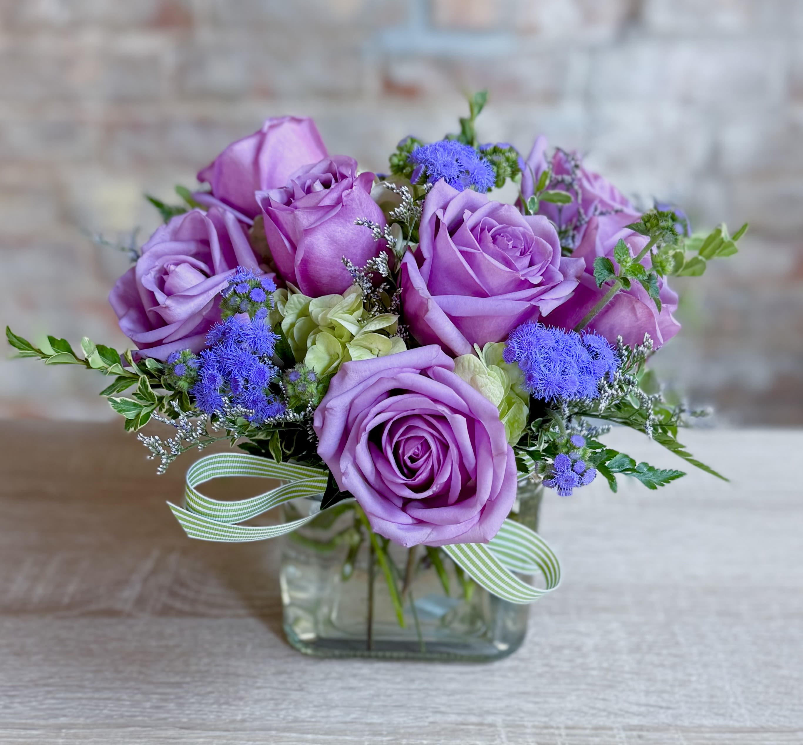 Norma Ann  - A clear glass 5” by 5” cube vase filled with a green hydrangea, 7 lavender roses and lavender filler. Soft and sweet! 