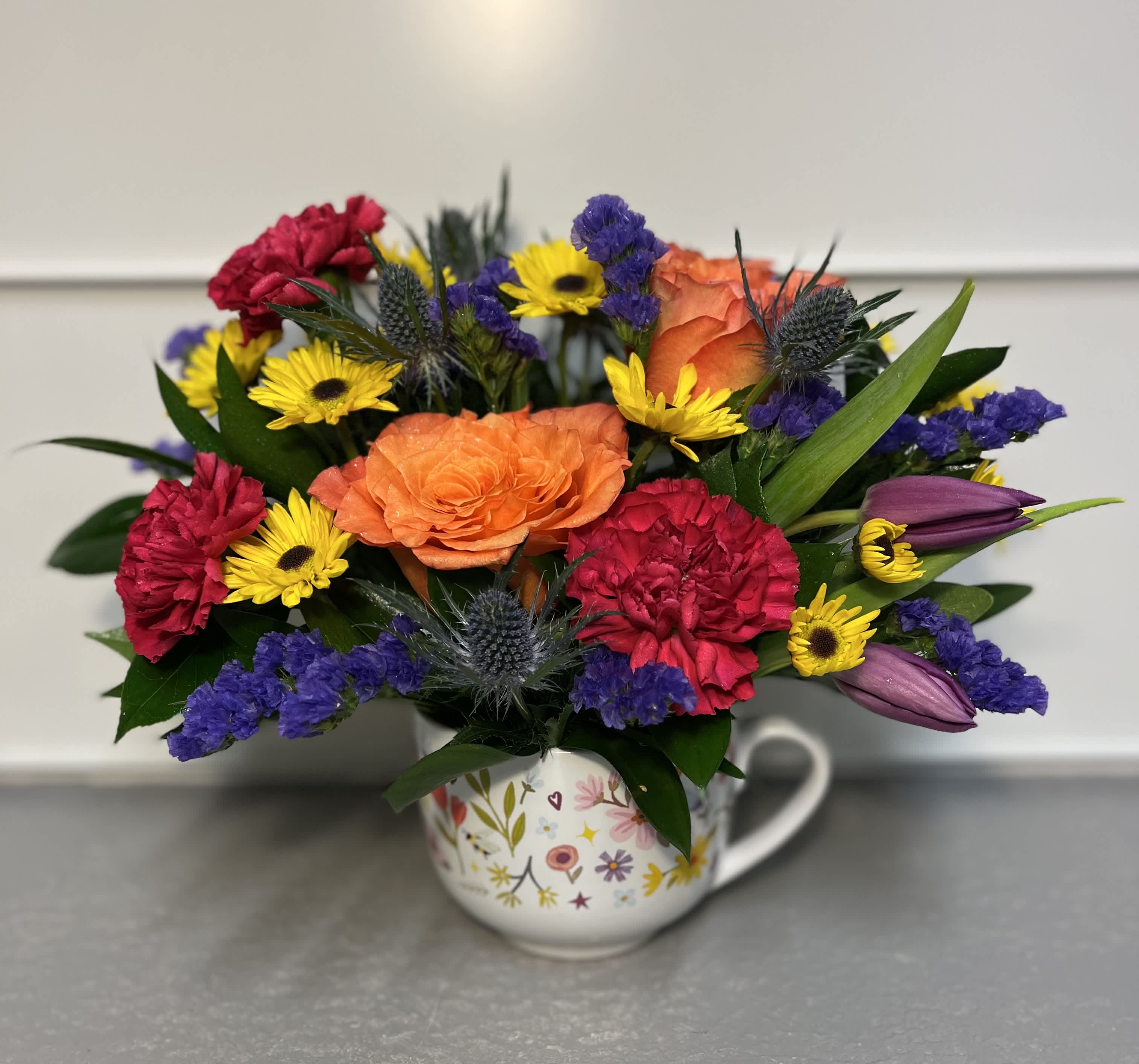 Happy Mug  - This cute little bouquet is made in a mug with greens, roses, carnations, tulips, eryngium, and viking palm daisies.  