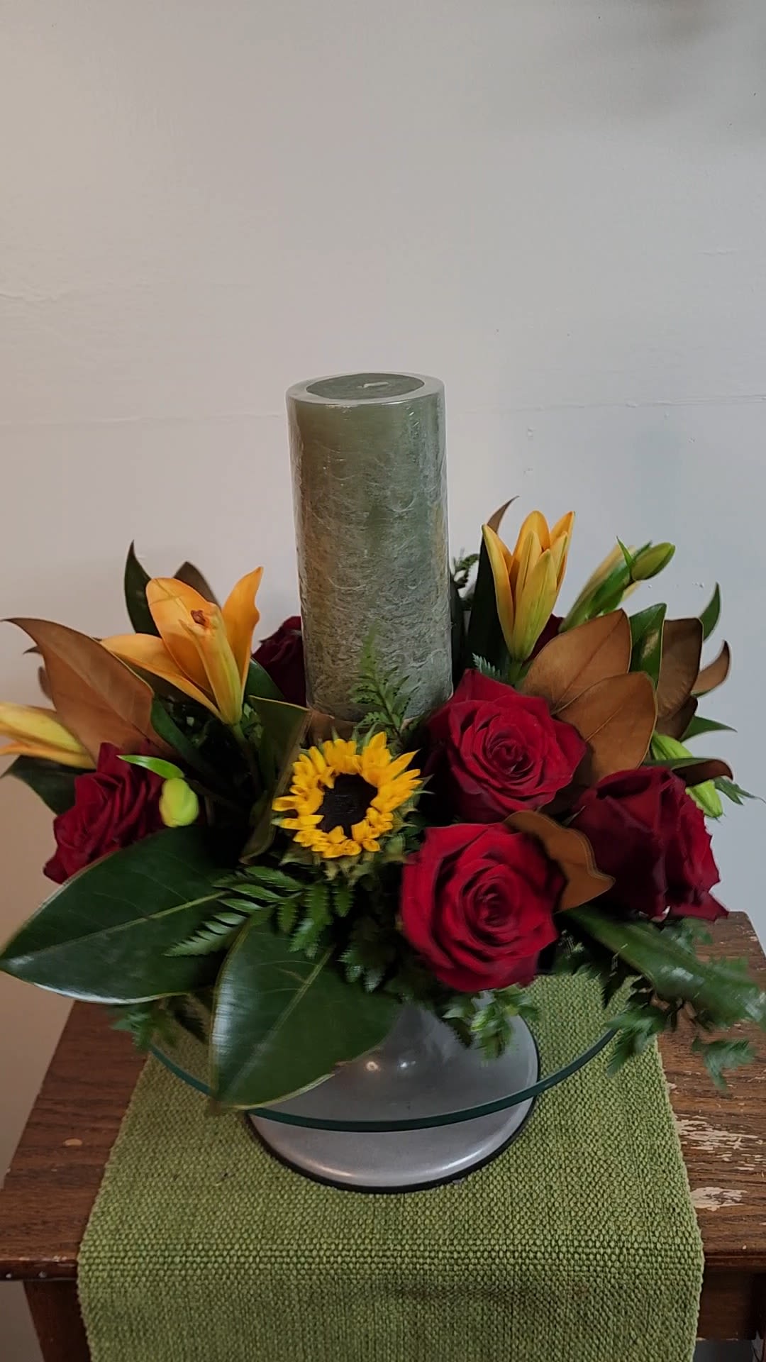 Piller of Elegance - Deep red roses, sunflowers, sweet lilies and magnolia leaves anchored by a single, unscented, long burning high quality candle is the perfect gift to adorne the table this season of thanks.