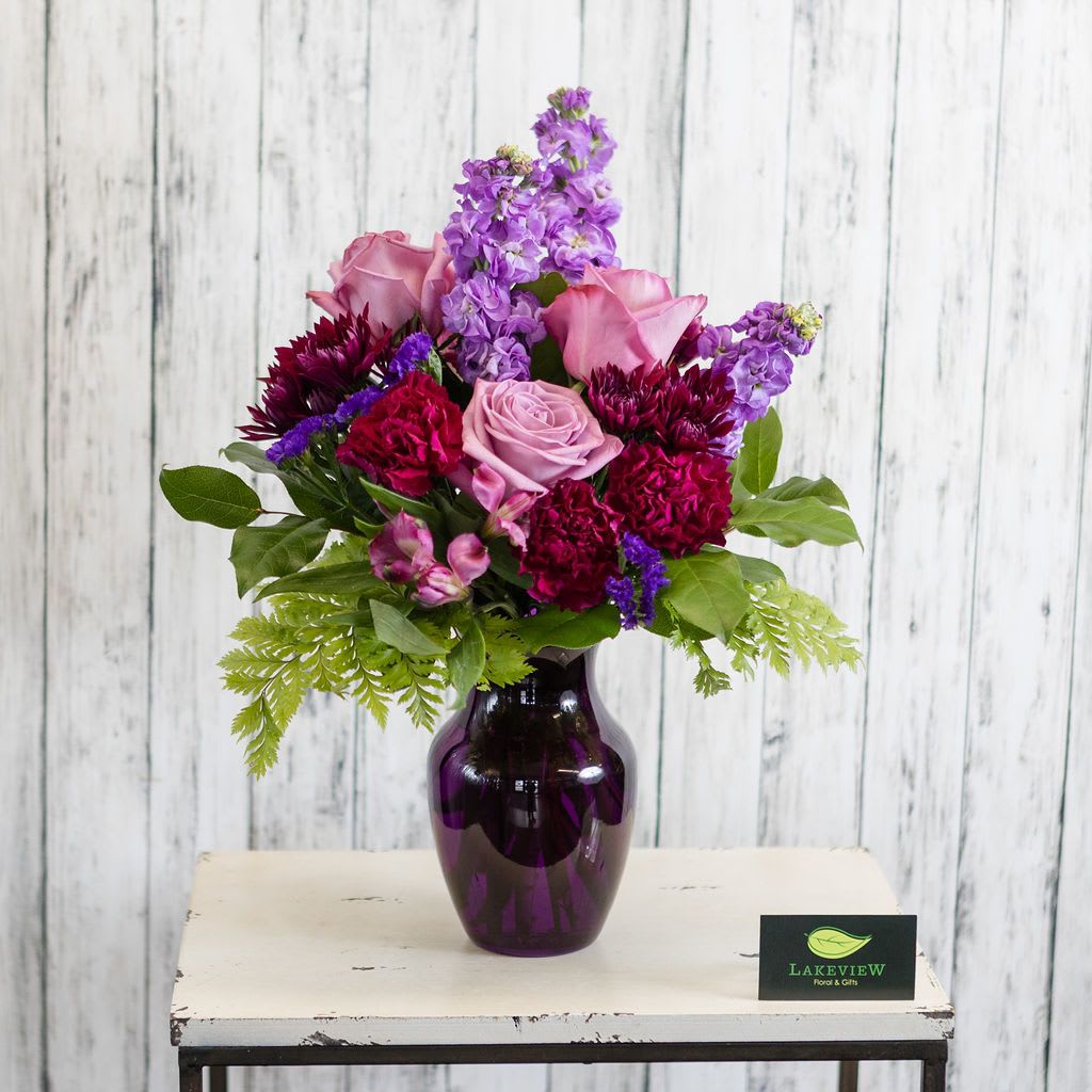 Violetta - Shades of purple blooms are presented in a purple glass vase.  Approximate Dimensions: 14&quot; W x 20&quot; H