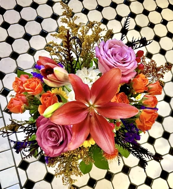 Fall Delight - Fall colors abound from this compact and delightful floral design. Orange Lillies, Purple Roses, celosia, berries, and other garden flowers are included in this wonderful seasonal arrangement.