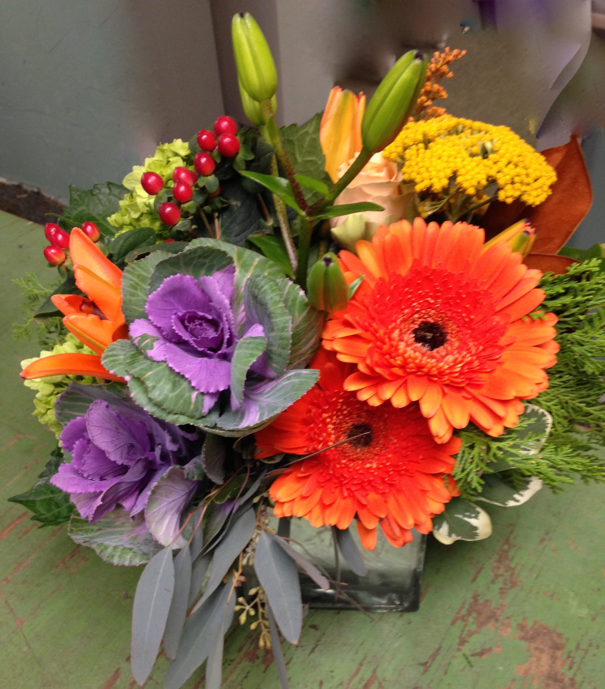 Harvest table - clear cube arranged with ornamental kale, gerbera daisies, lillies,  hypericum berries, roses and more.