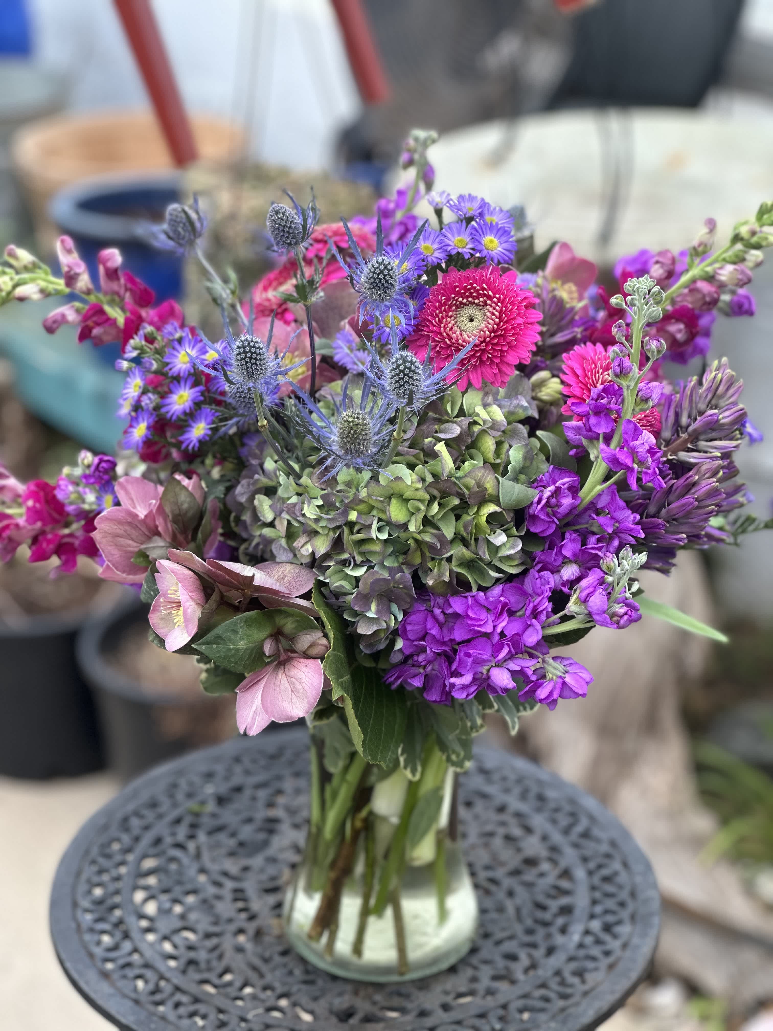 The Barrymore - This arrangement is a very modern take on the deep colors that purple reflects against the deep green of the orchids. Lush green cymbidium orchids, purple calla lily's, green hydrangea purple lisianthus,  purple stock , with a swirl of aspidistra to finish off the vase. 