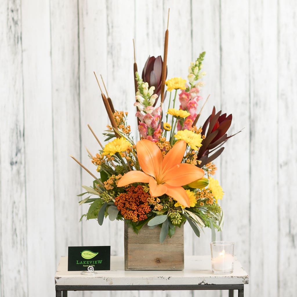 Radiant - Orange lilies, fall mums and snapdragons glow with the colors of autumn in a wooden branch vase.