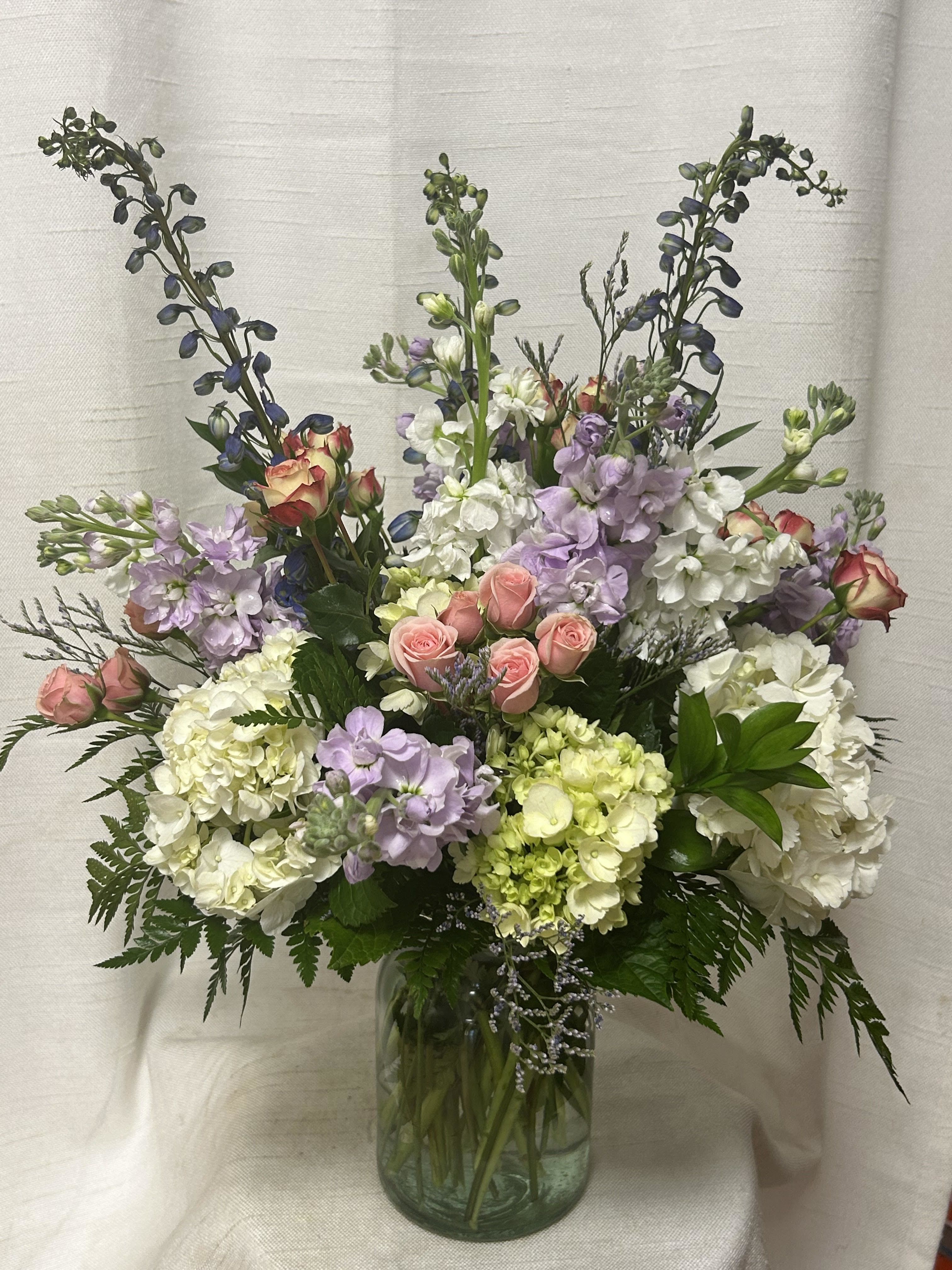 Tranquil Oasis (BR) - Step into a whimsical realm with our &quot;Tranquil Oasis&quot; floral arrangement, a magical creation inspired by the allure of a mystical garden in full bloom. This enchanting ensemble features a captivating combination of delicate pink roses, lush green and white hydrangea, fragrant purple stock, and graceful blue delphinium.