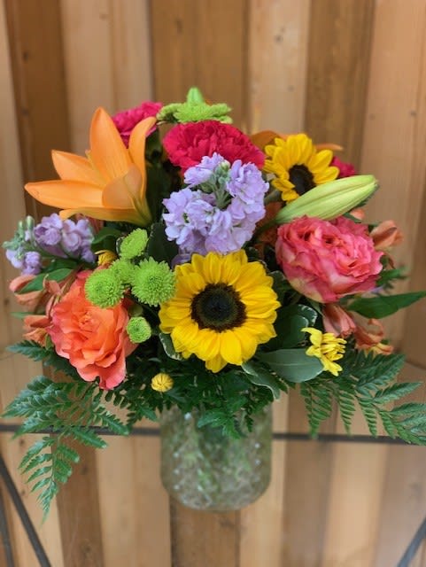 Vivid Floral Masterpiece - Bright &amp; Beautiful Vase Arrangement – Sunflowers, Lilies, Carnations and Roses  Bring a burst of color and joy into any space with our stunning fresh flower vase arrangement from Haehn Florist &amp; Greenhouses in Wapakoneta, Ohio. Hand-designed by our talented floral team, this vibrant bouquet features a cheerful mix of Sunflowers, Lilies, Carnations and Roses. Perfect for birthdays, anniversaries, get well wishes, or simply to brighten someone’s day, this arrangement is overflowing with freshness and charm.  Each stem is carefully selected for quality and beauty, then artfully arranged in a classic glass vase for a timeless look. Whether delivered to a loved one or enjoyed in your own home, this bouquet makes a lasting impression.   Why Choose Haehn Florist &amp; Greenhouses?  Locally owned and trusted for premium flowers in Wapakoneta, OH  Same-day flower delivery available in Wapakoneta and surrounding areas  Personalized service with every order   Visit Us: Haehn Florist &amp; Greenhouses, 410 Hamilton Rd, Wapakoneta, OH 45895  Call Us: 419-738-8485  Brighten life’s moments with this unforgettable mix of sunflowers, roses, gerbera daisies, and hydrangeas—expertly designed and delivered with care.