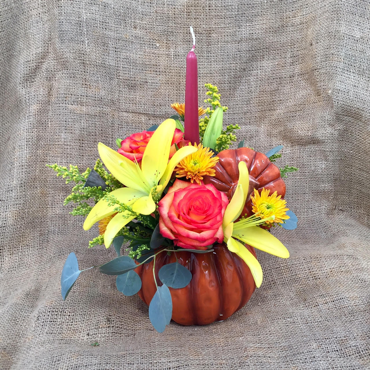 Autumn Splash Centerpiece - A festive arrangement of bright fall flowers, such as roses, lilies, chrysanthemums, and solidago, in a ceramic pumpkin dish.