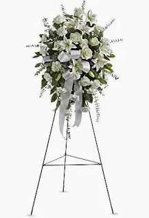 Sentiments of Serenity Spray - ***MUST BE ORDERED 3 BUSINESS DAYS IN ADVANCE. PLEASE CALL US DIRECTLY TO SEE ABOUT SOONER ACCOMMODATIONS.***   Beautifully simple, this lovely spray of white roses, lilies and carnations decorated with white satin ribbon is a tasteful way to express your sympathy. The elegant spray includes white roses, white Asiatic lilies and white carnations, accented with assorted greenery.  PICTURE IS THE DELUXE VERSION  