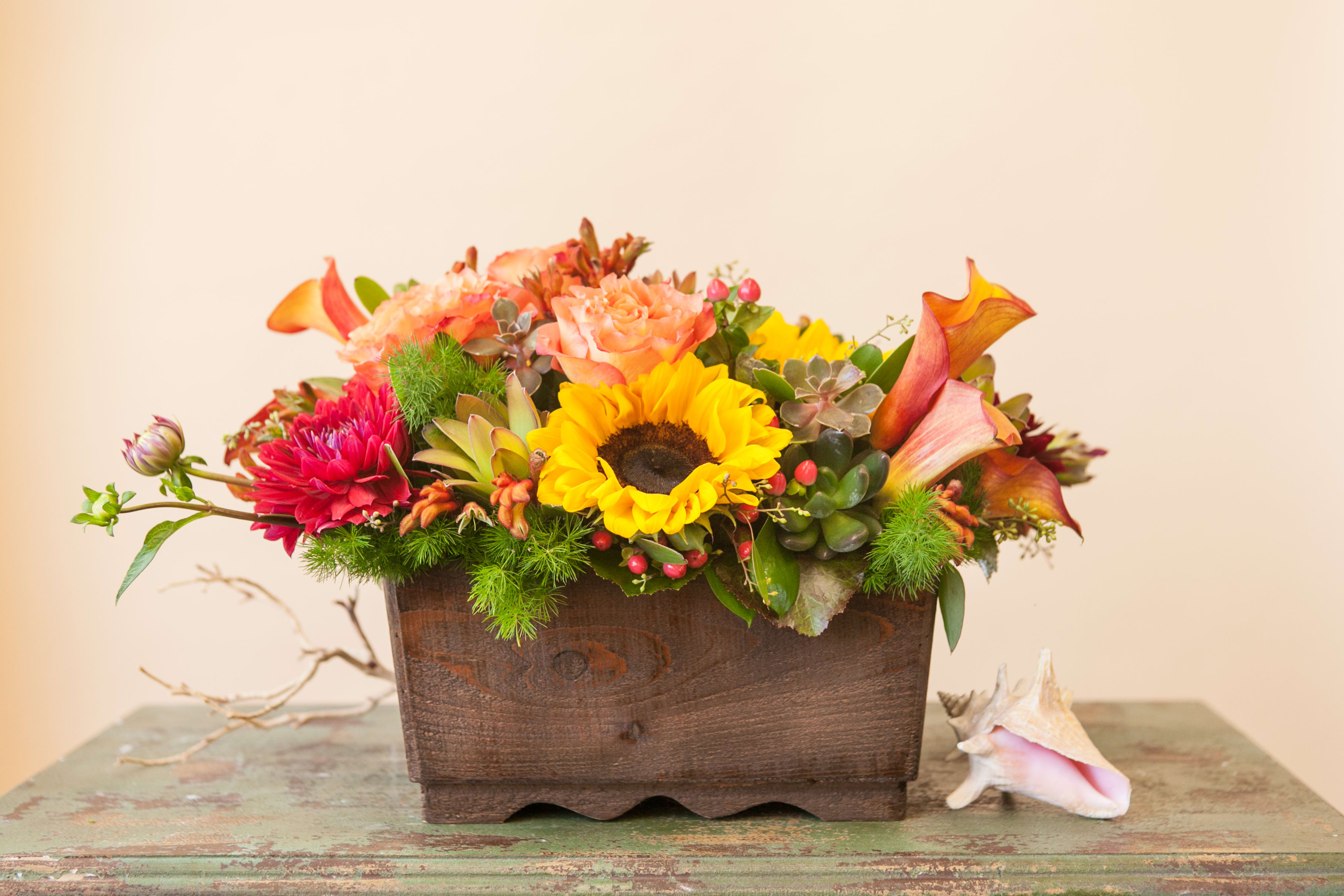 Amber Lantern - Stunning sunset colored flowers arranged in a large, reusable wooden container- including roses, sunflowers, hypericum, and succulents, all complimented with unique greenery and seasonal flowers. This is a gorgeous statement piece that will bring the elegance of fall to your space.   Flowers may vary, please call if this is a concern.