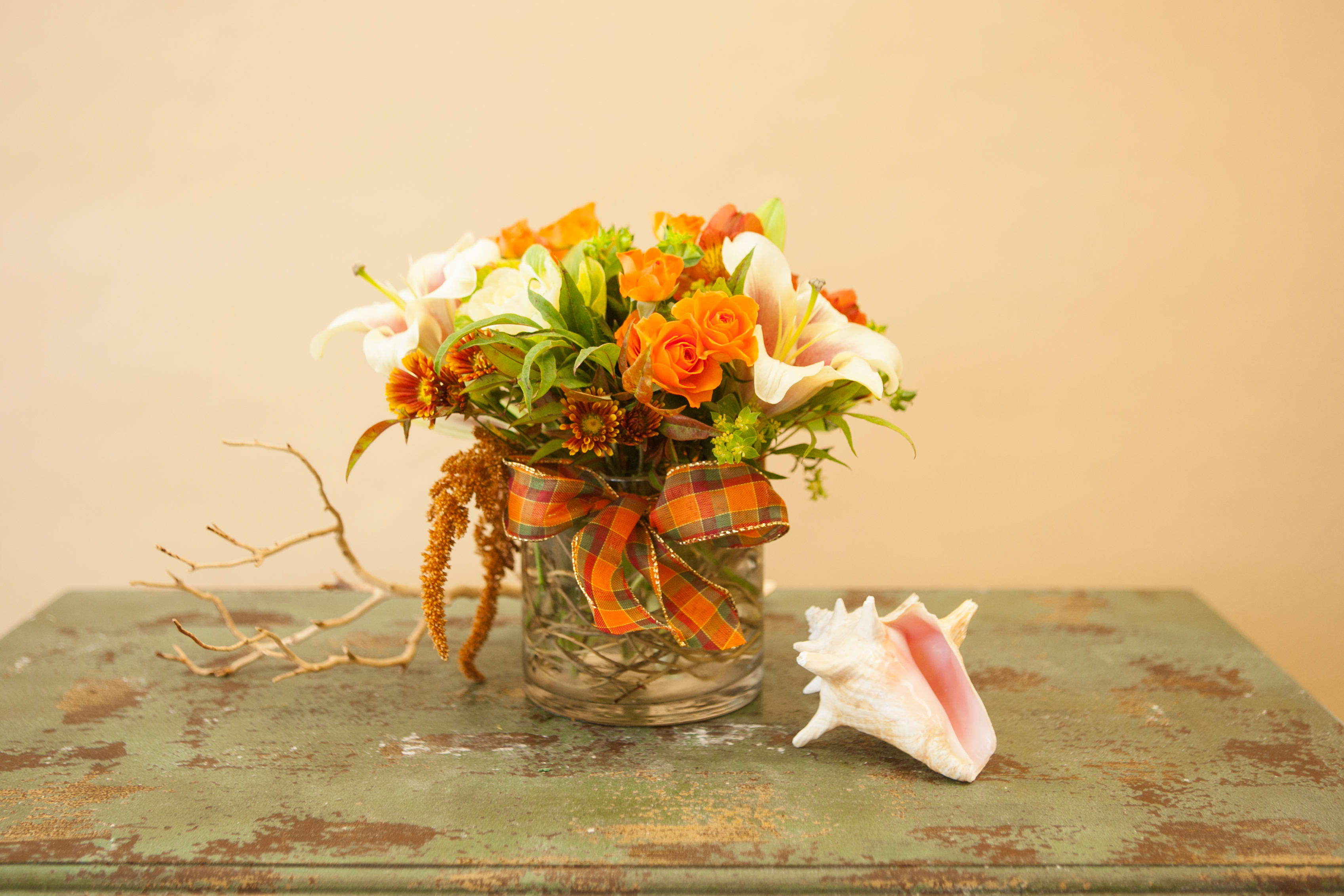 Autumn Bliss - A sweet arrangement of spray roses, lilies, alstroemeria and other autumn colored flowers all arranged in a clear glass cylinder vase with willow branches inside. Flowers and bow color may vary from week to week, please call if this is a concern.