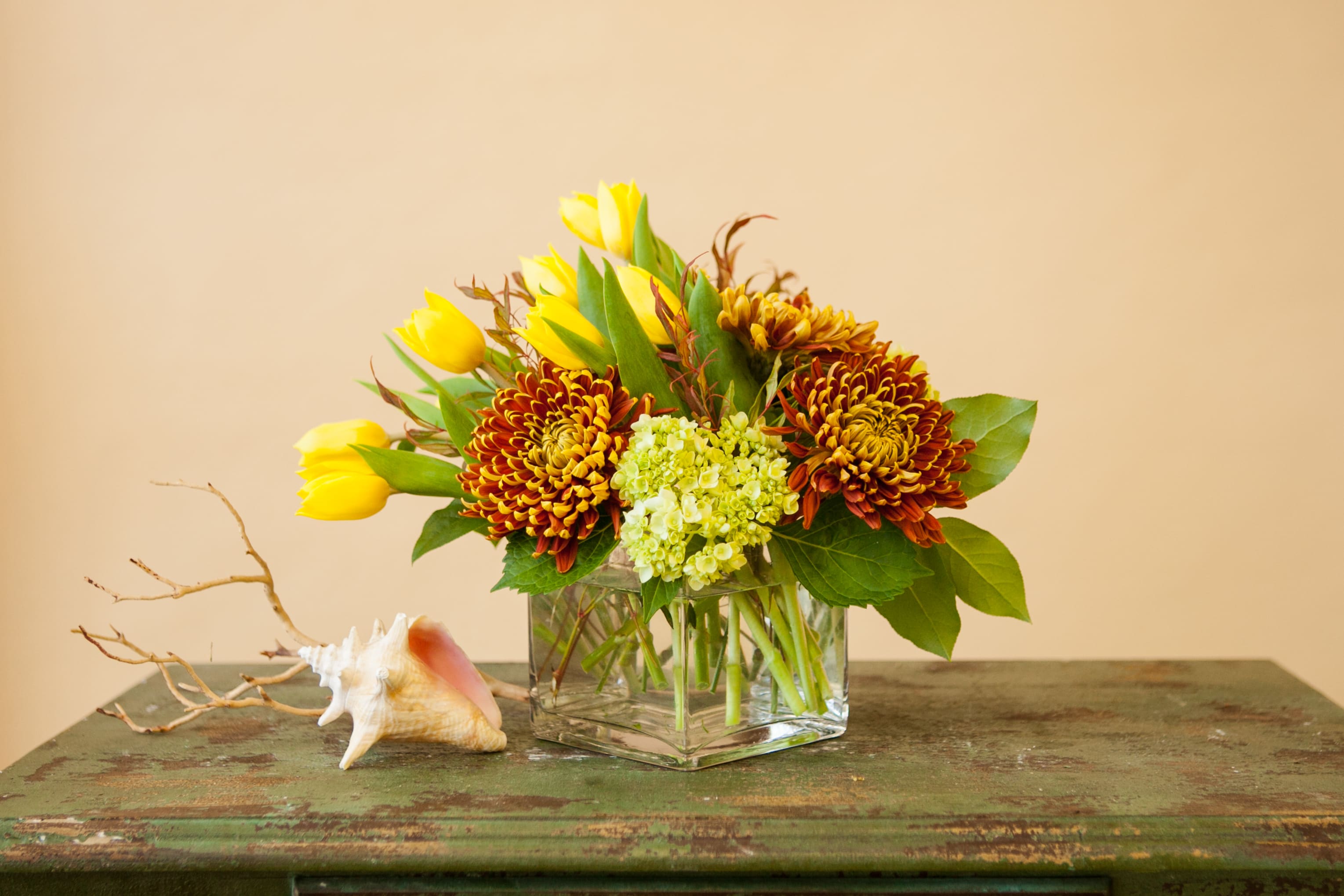 Fall Fantasy - A unique fall arrangement of tulips, hydrangea and spider mums arranged in a contemporary style in a clear glass cube vase. Colors will vary from week to week, please call if this is a concern.