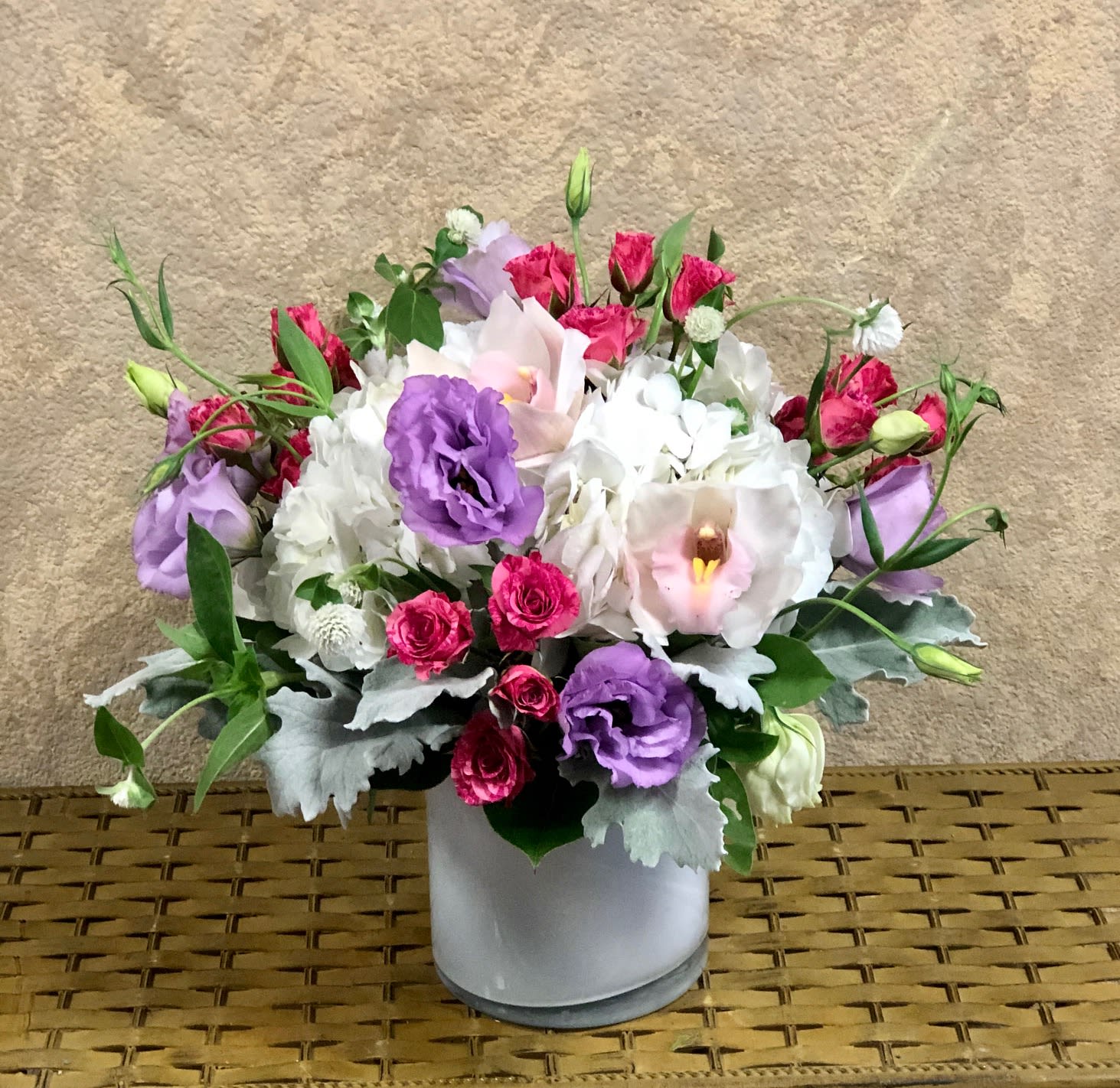 Sweet Valencia Living - Recipe: White Hydrangeas, Purple Lisianthus, White Orchids, Hot Pink Roses. Cylinder Crystal White vase.  Availability: All year round Design View: Symmetric Front Facing View Photo shown: Standard