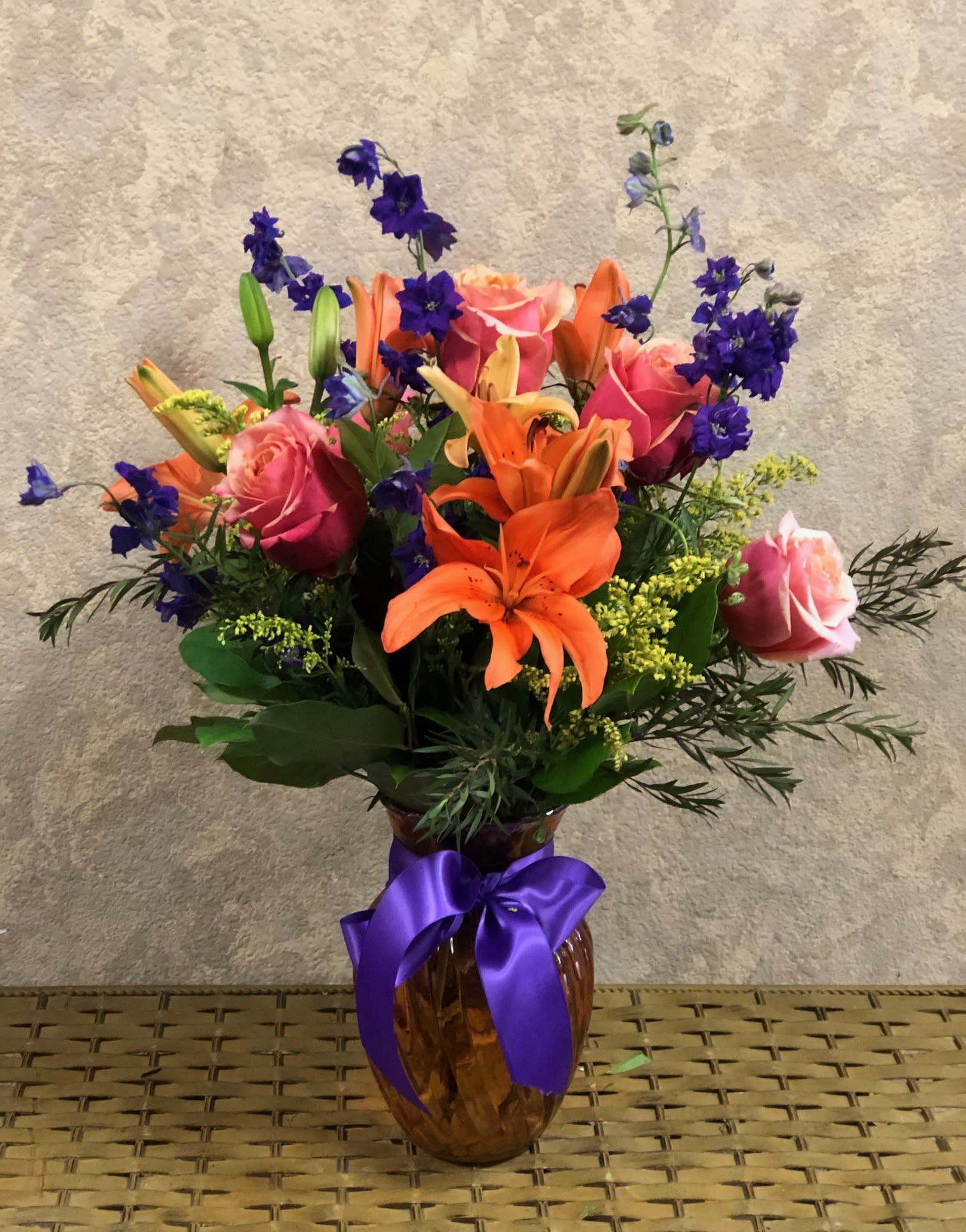 Color My World Color My World - Type of Flowers: Orange Lilies, Orange Roses, Purple Larkspur, and greens in an Orange Vase. Availability: All year round Substitute Available: Yes Design View: All Facing View Photo shown: Regular