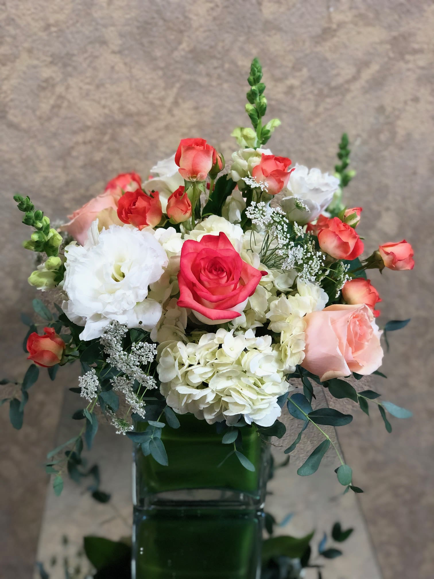 Georgia Peaches  - Send someone special this beautiful coral and peach arrangement.  Type of Flowers: The arrangement includes White Hydrangeas, Peach Roses, Lisianthus, Snapdragons, Coral Spray Roses, and Queen Anne's lace in a short clear leaf-wrapped vase.  Availability: All year round Substitute Available: Yes Design View: Symmetric Front Facing View Photo shown: Regular 