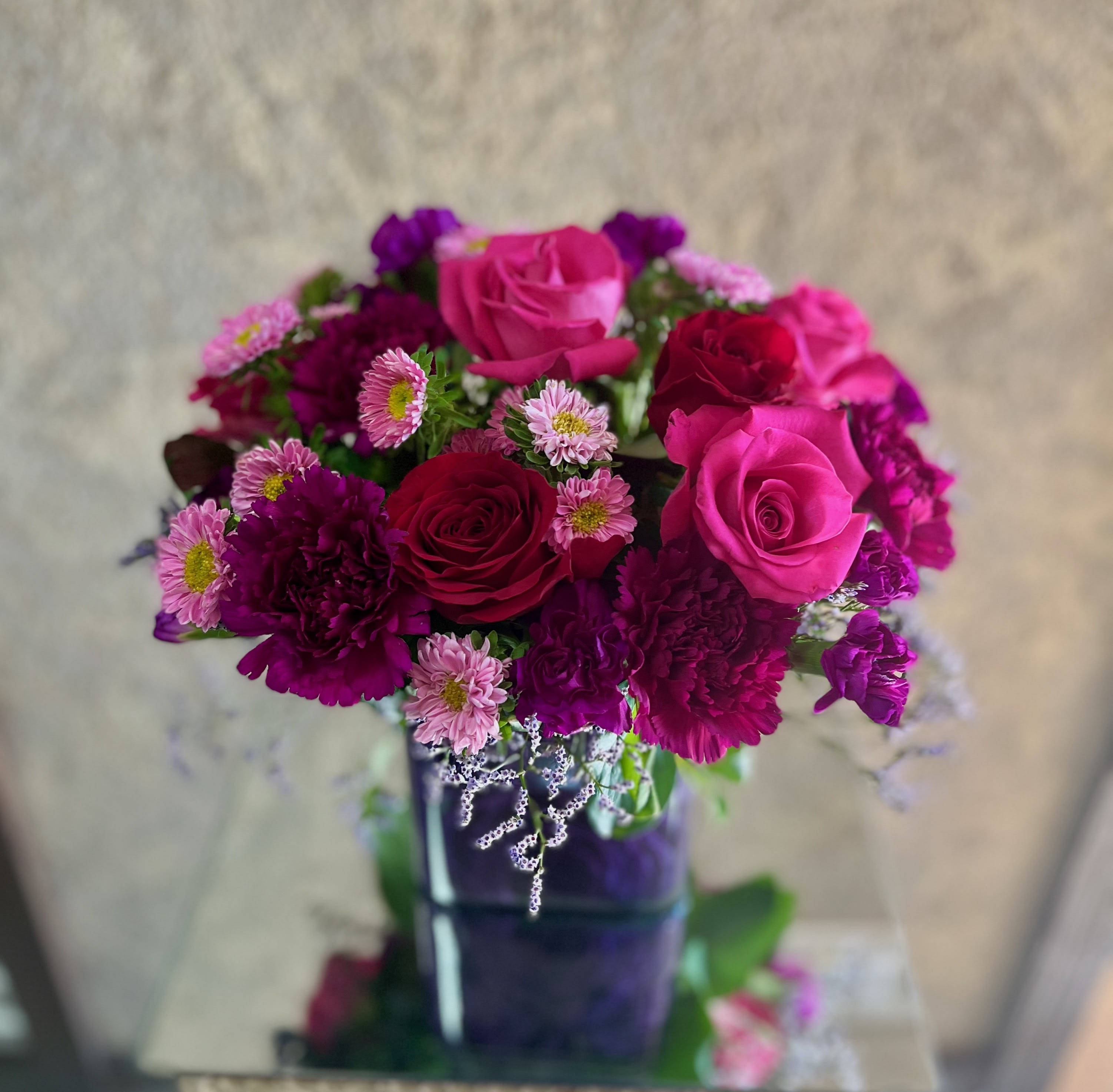 Bejeweled Beauty - Our top-seller is filled with romantic colors including hot and light pink with shades of dark purple and reds blooms. Recipe: Hot pink roses, dark red spray roses, purple carnations and pink miniature carnations are accented with assorted greens in a cubed vase with purple wrap. Seasonal: All year round Design View: All Facing View Photo shown: Standard