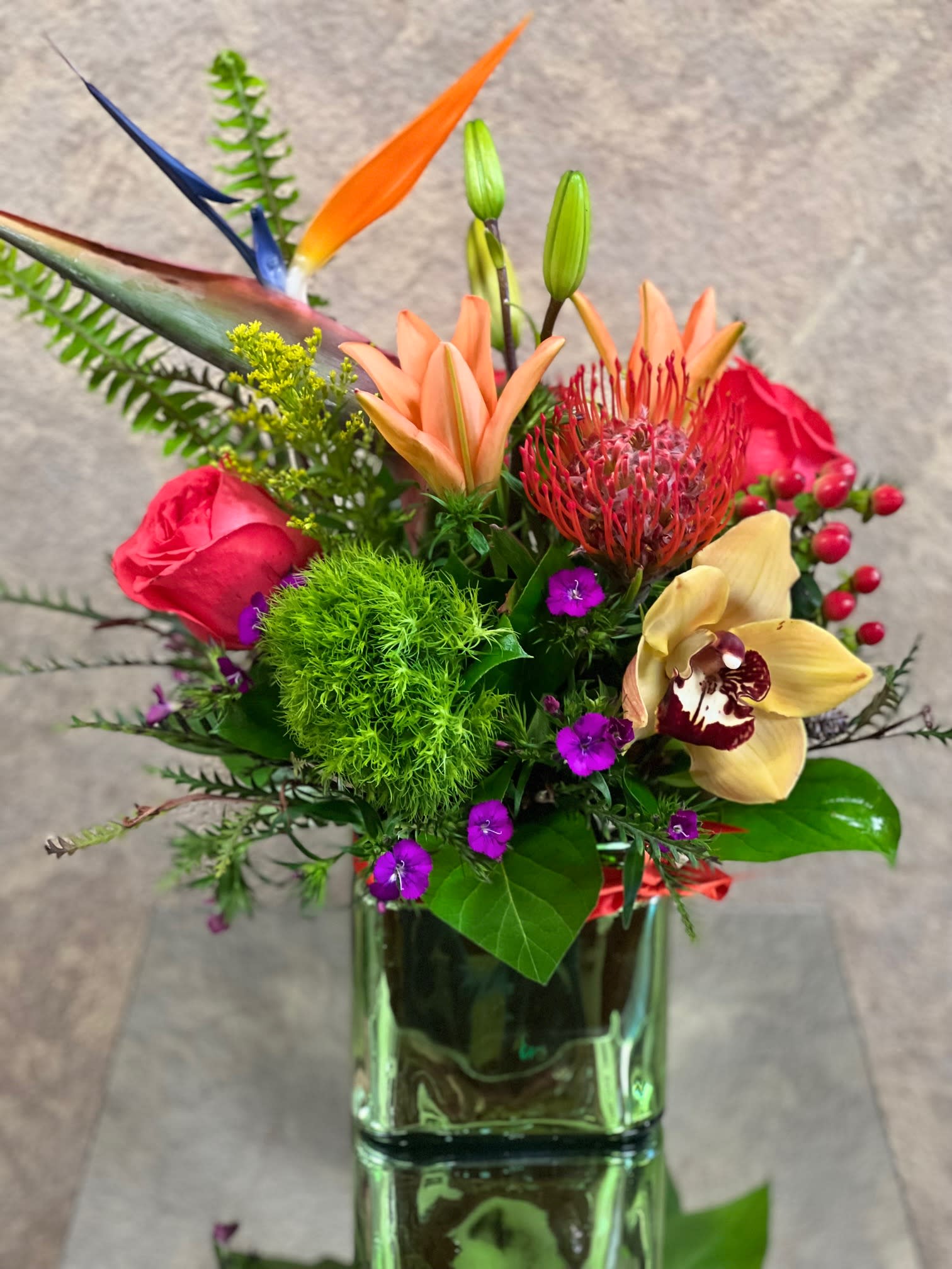 Touch of Paradise - Send a Touch of Paradise to someone special, this arrangement includes orange lilies, lilies, bird of paradise, protea, orchids, and sweet William in a square vase with an orange ribbon.