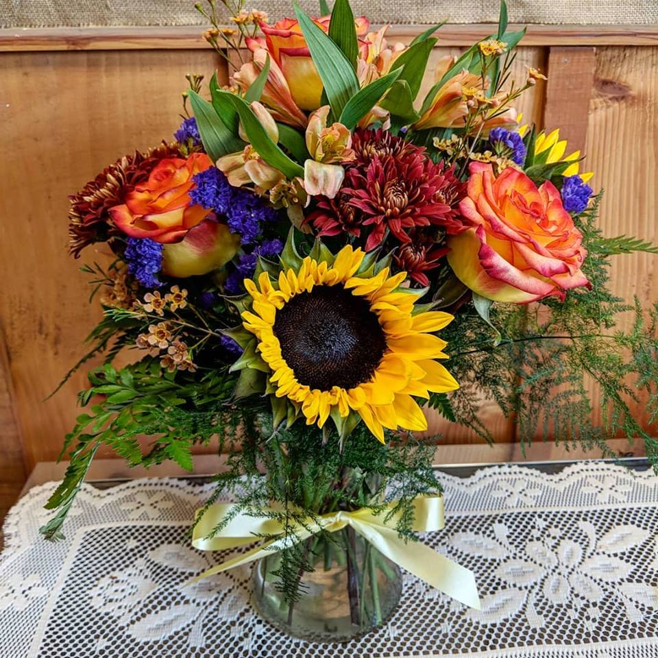 BeautiFall Dreams - Fairy tale greens enhance a stylish glass vase and the fiery colors of orange, yellow and burgundy roses, sunflowers, alstroemeria and mums will have you dreaming of bonfire nights under the starry purple status and make this fall favorite the arrangement of your dreams.