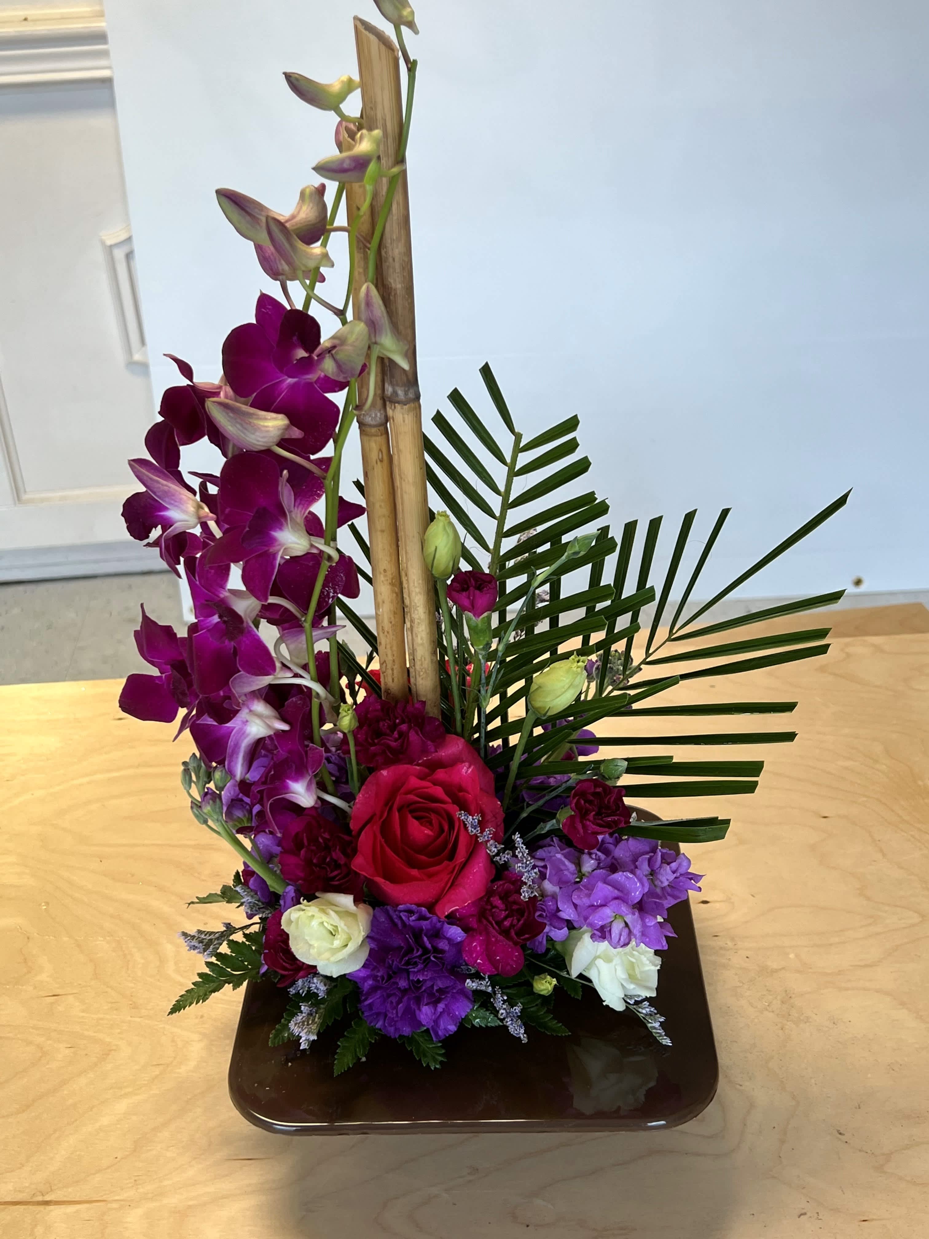 Zen Artistry Zen Artistry - An earth-tone container and exotic palm leaf provide the perfect backdrop for purple orchids and a mix of delightful tropical flowers. We may substitute orchid color based on availability. Please note: Flower varieties and colors may be substituted based on seasonal and daily availability. We always ensure your arrangement is of equal or greater value and just as beautiful.