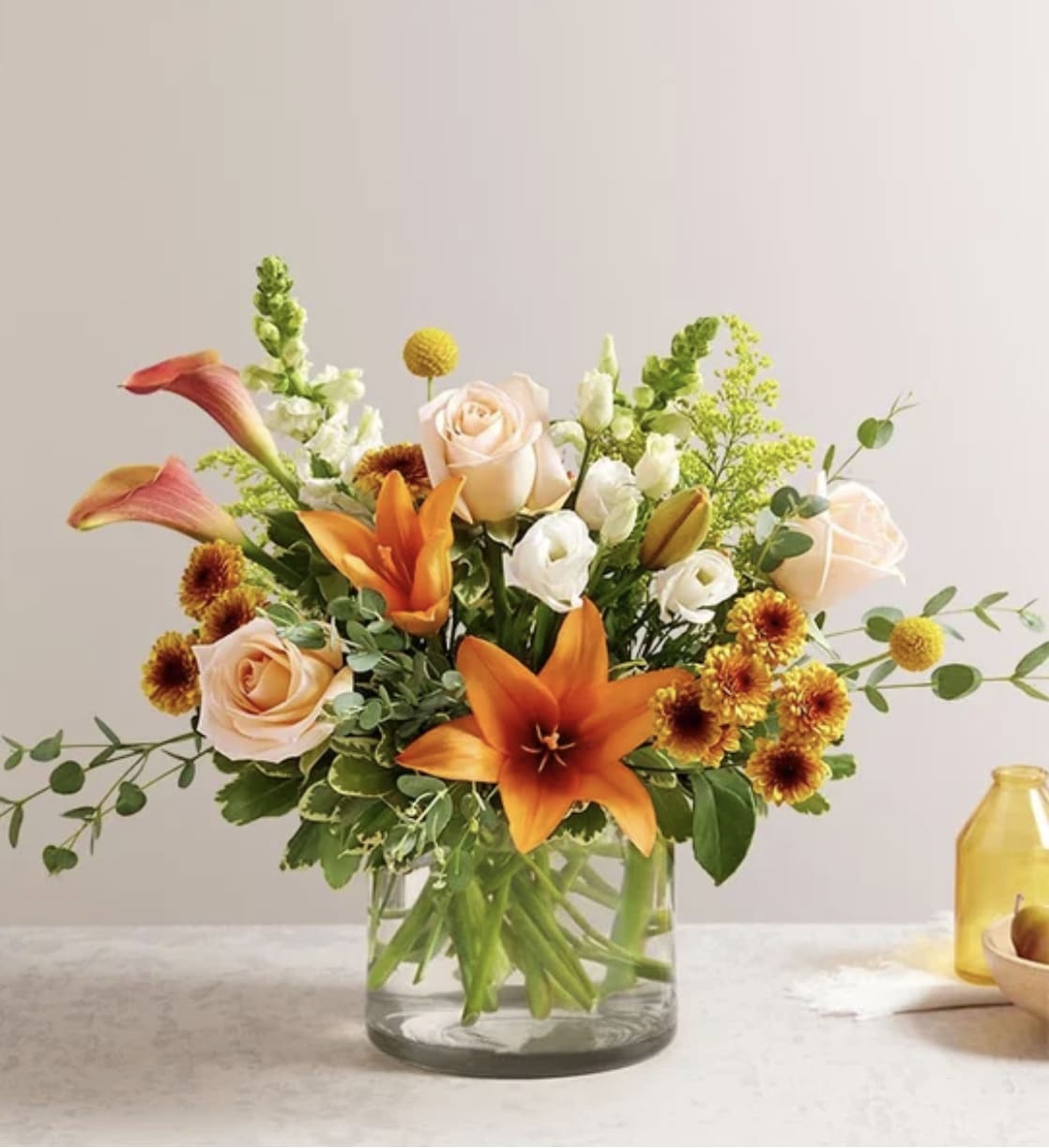 Autumn Amazement Bouquet - Our nature-inspired bouquet captures all the amazement of autumn. Highlighted by unique, textural yellow craspedia, with rich tones of orange, peach, bronze and white, this loosely gathered arrangement arrives in a cylinder vase to brighten every gathering with beauty and charm. VASE WILL VARY