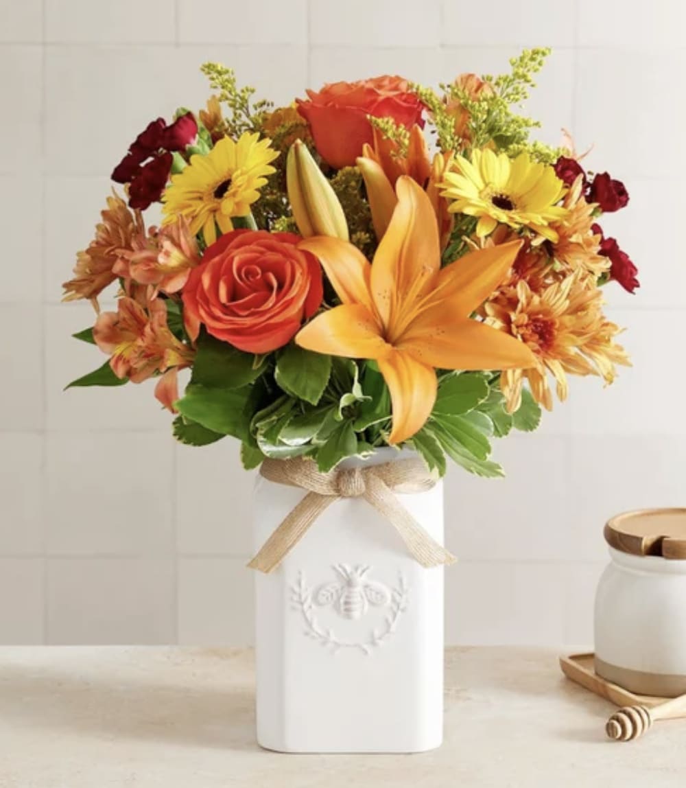 Honey Bee Buzz for Fall - Get them buzzing for fall! Our unique, stylized bouquet is gathered with a mix of blooms in warm yellow, orange, bronze and burgundy. Designed in our Sweet As Can Bee artisanal vase, featuring an adorable honey bee and raffia bow, it’s a gift that adds seasonal beauty to any decor.