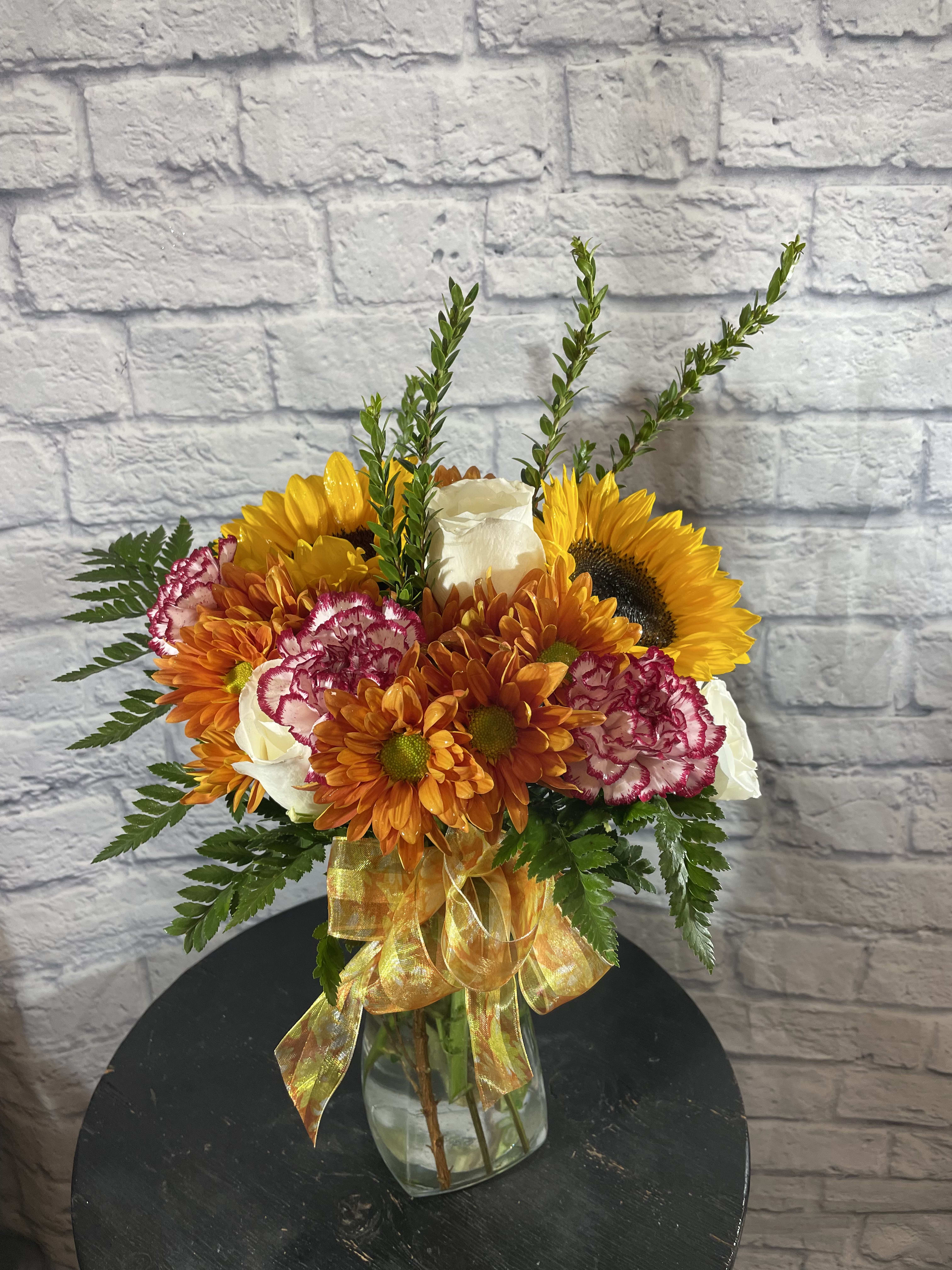 Fall Look  - Who loves fall colors? the bouquet is for those who love those fall colors and ROSES!  This floral design will a mixture of fall colors and come with 3 roses. It comes with locally grown sunflowers (may vary in colors: regular yellow, red, or teddy bear variety) and fresh greenery.  Always Fresh and Seasonal Flowers from Local Farmers.   We love to give our florist the ability to create as they please, flower type, vases and colors may vary depending on inventory.   Delivery available to the cache valley area.