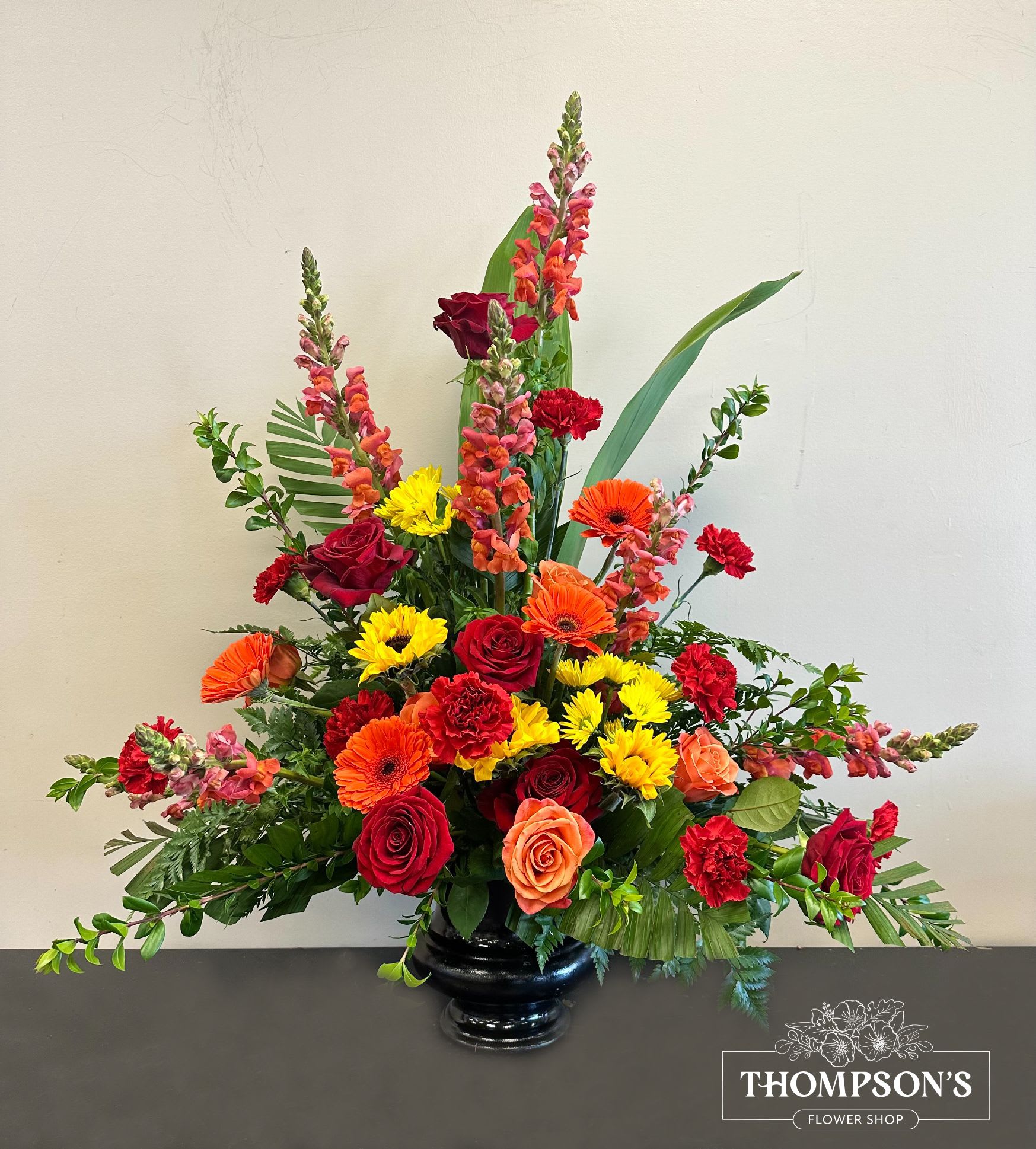 Ceremony Arrangement CV-26 Ceremony Arrangement CV-26 - Radiating warmth and vibrancy, this ceremony arrangement features a cheerful mix of orange snapdragons, red and orange roses, bold gerbera daisies, and yellow mums. Designed to celebrate a life lived fully, it brings a burst of color and uplifting energy to the service, offering comfort and remembrance through nature’s brightest blooms.