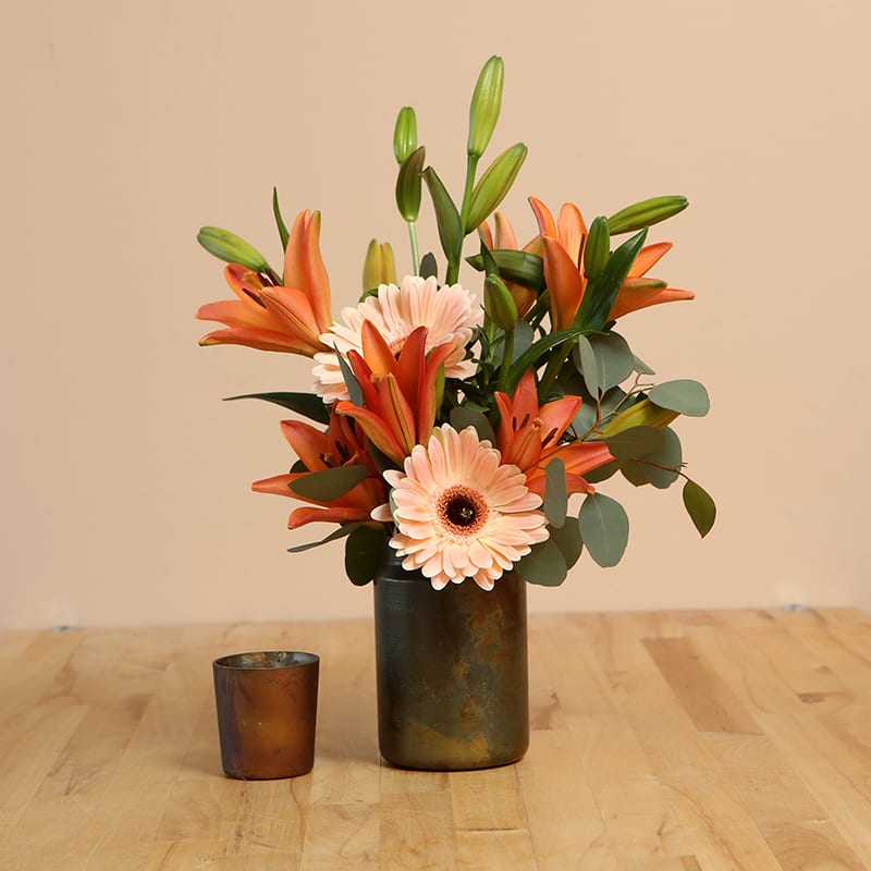 Peachy Keen - Let our bouquet of lovely peach and orange lilies let your recipient know everything is all right! Gorgeous Asiatic lilies emerge from a lovely patinated metal container, joined by Gerbera daisies and eucalyptus for fun. Beautiful from every angle.  Lilies, Gerberas, and seasonal greens arranged in an unique patinated metal container. Approximately 20&quot;H x 12&quot;W.