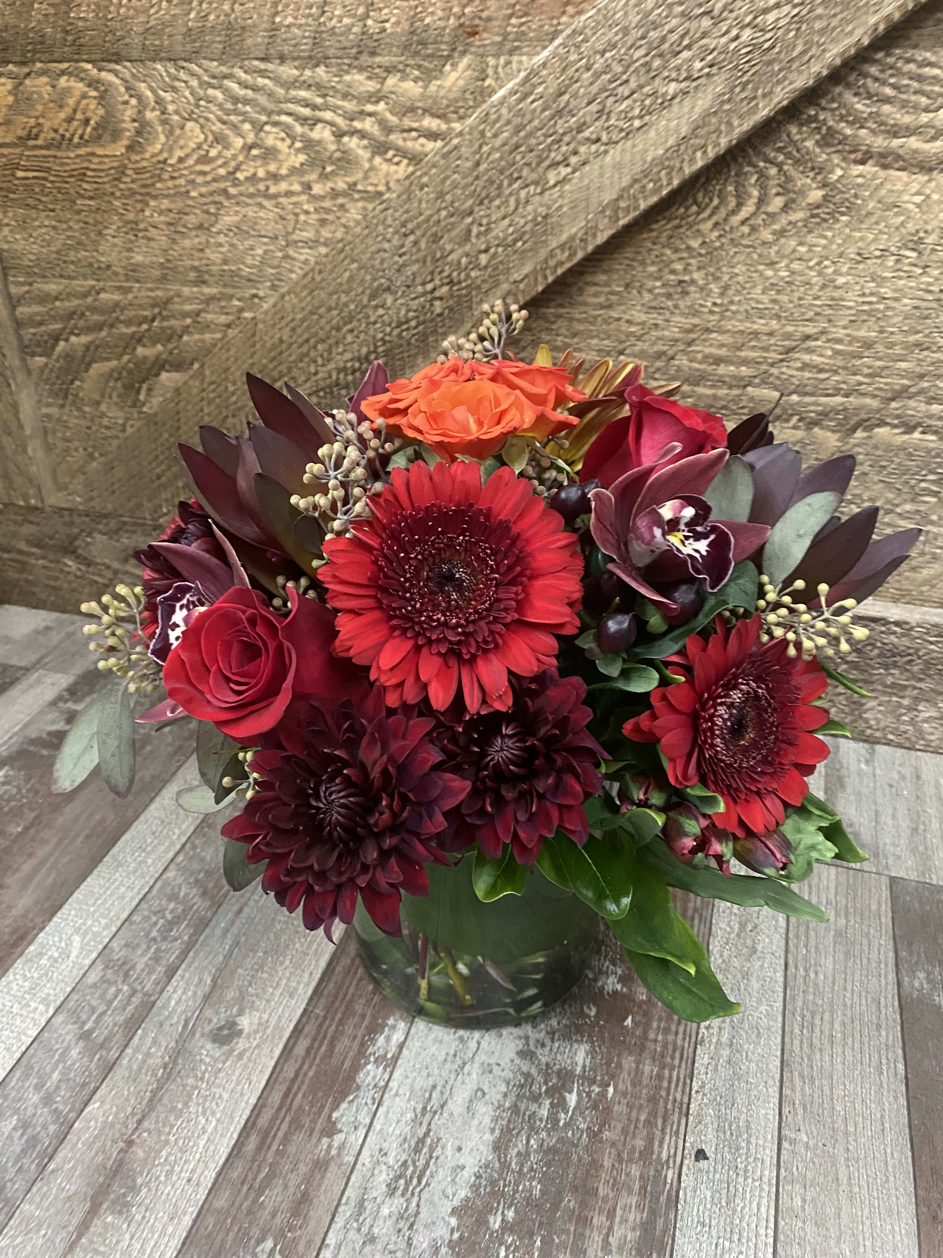 Burgundy Delight  - A beautiful design consisting of only burgundy and red toned flowers. We will add different textures of greenery such as eucalyptus and ruscus to break up a bit.  Flowers arrive in a clear glass leaf wrapped vase. 