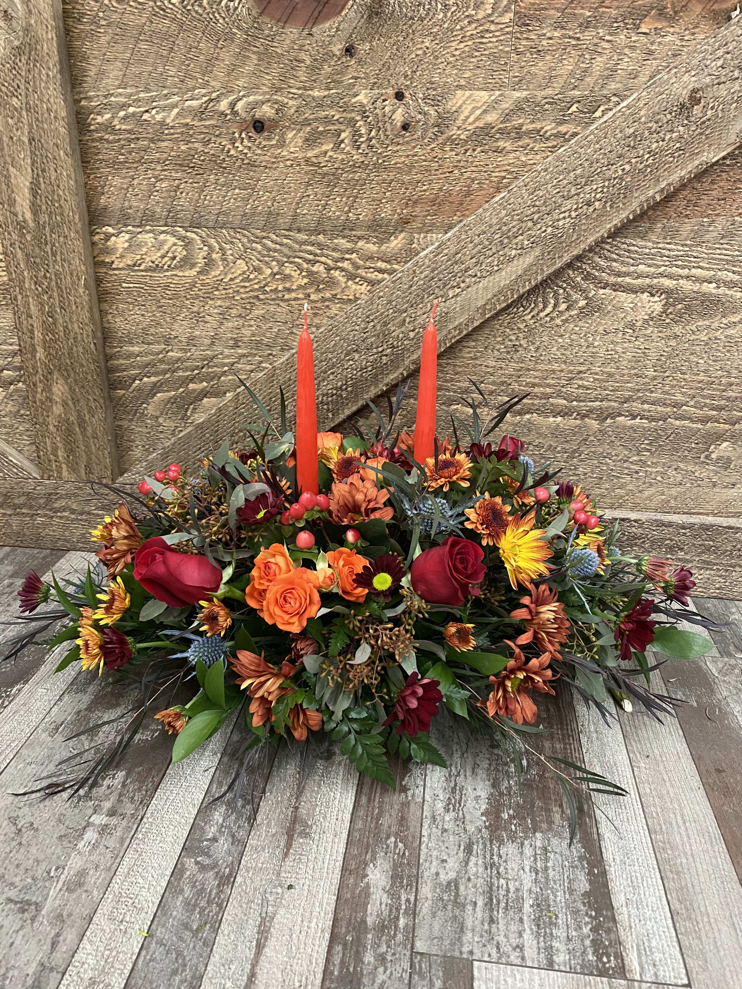 Traditional centerpiece with candles - This traditional holiday centerpiece is designed with mums, roses, berries and mixed greens. Perfect for a long table. Version shown is the deluxe. 