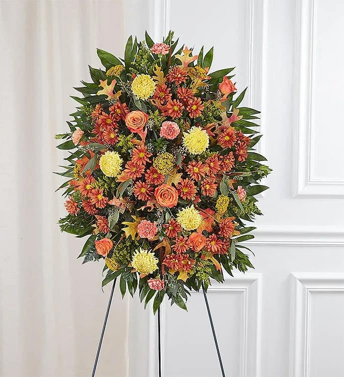 Standing spray fall colors  - This beautiful standing spray captures the warmth and richness of the season, offering a heartfelt tribute to a life well lived. Designed with a stunning blend of fall-colored blooms — including orange roses, rust and bronze chrysanthemums, golden carnations, and lush greenery — it’s accented with seasonal foliage for a natural, comforting touch. Perfect for funeral services or memorial ceremonies, this vibrant arrangement symbolizes gratitude, cherished memories, and the enduring beauty of a loved one’s legacy.