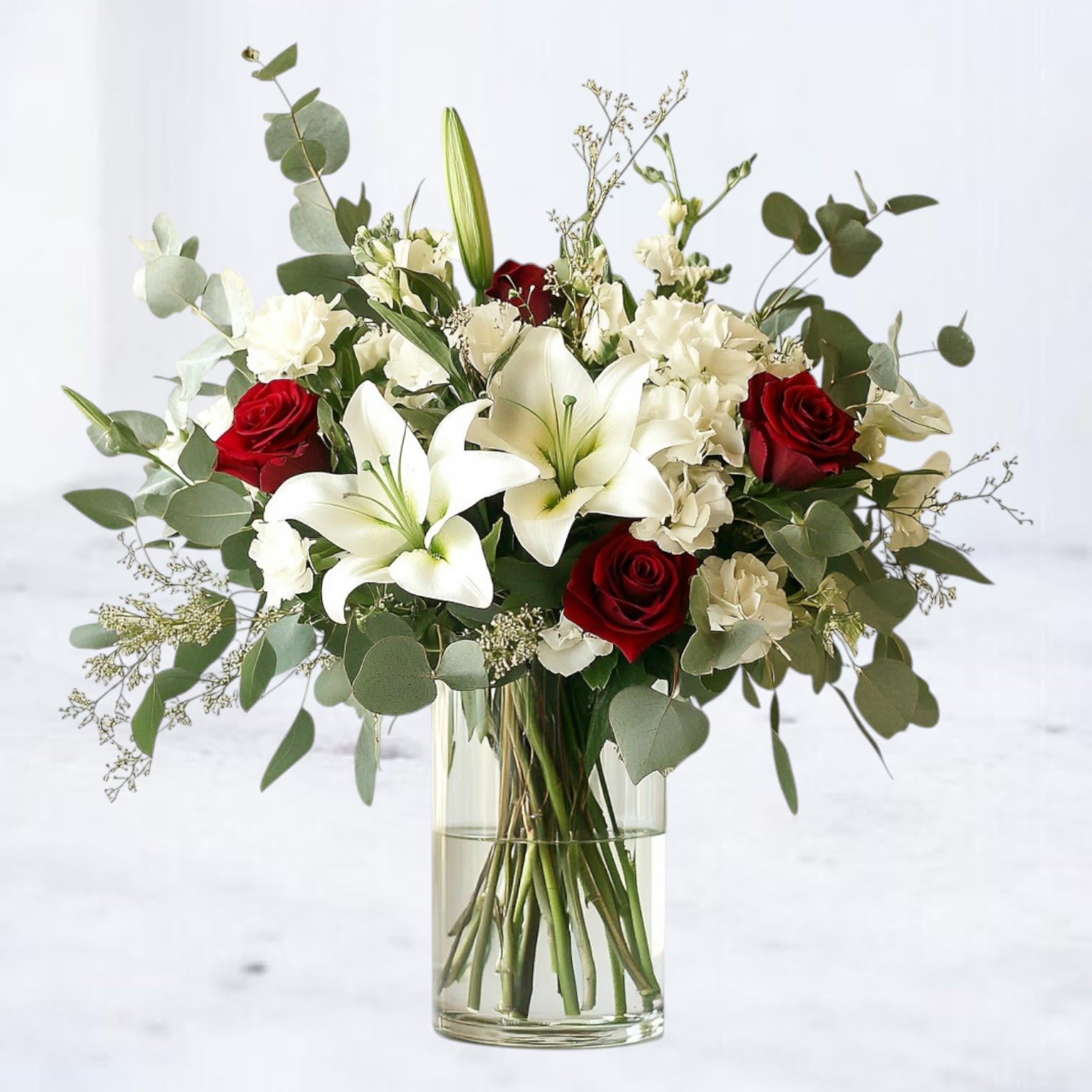 Ever After Ever After - Celebrate a love that stands the test of time with Ever After, a stunning arrangement of velvety red roses, graceful white lilies, and lush greenery. Each stem is thoughtfully chosen to symbolize passion, purity, and enduring devotion, making this bouquet a timeless gift for anniversaries, weddings, or any romantic milestone. Handcrafted by our skilled florists, this design is presented in a tall glass vase for an elegant, ready-to-display gift. With same-day delivery available in Houston, Magnolia, The Woodlands, and surrounding areas, your heartfelt gesture will arrive fresh and unforgettable. Perfect For: Anniversary surprises Romantic celebrations Elegant “just because” moments Order Today and let your love story bloom beautifully.