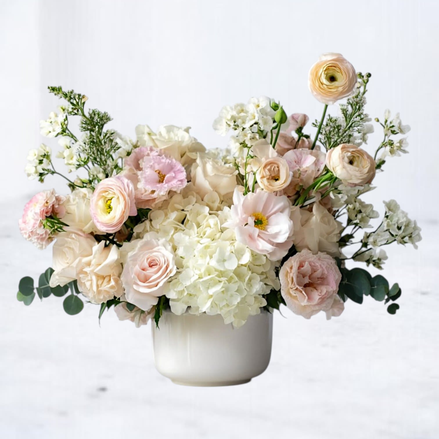 Cameo Embrace Cameo Embrace - Offer comfort and gentle beauty with our Cameo Embrace arrangement — a serene sympathy bouquet designed to honor loved ones with grace. Featuring soft white hydrangea, blush roses, ranunculus, and lisianthus, this arrangement exudes peace, remembrance, and tender love. Arranged in a modern white ceramic vase, it provides a comforting presence for funeral services, memorials, or as a heartfelt gift delivered to the home. Available for sympathy flower delivery in Magnolia, The Woodlands, Spring, Conroe, and throughout the Greater Houston area. Send this elegant pastel floral tribute as a thoughtful way to express condolences and bring warmth to grieving hearts. Elegant condolence flowers Same-day sympathy flowers Houston area Pastel funeral floral arrangement Comforting flowers for memorial services