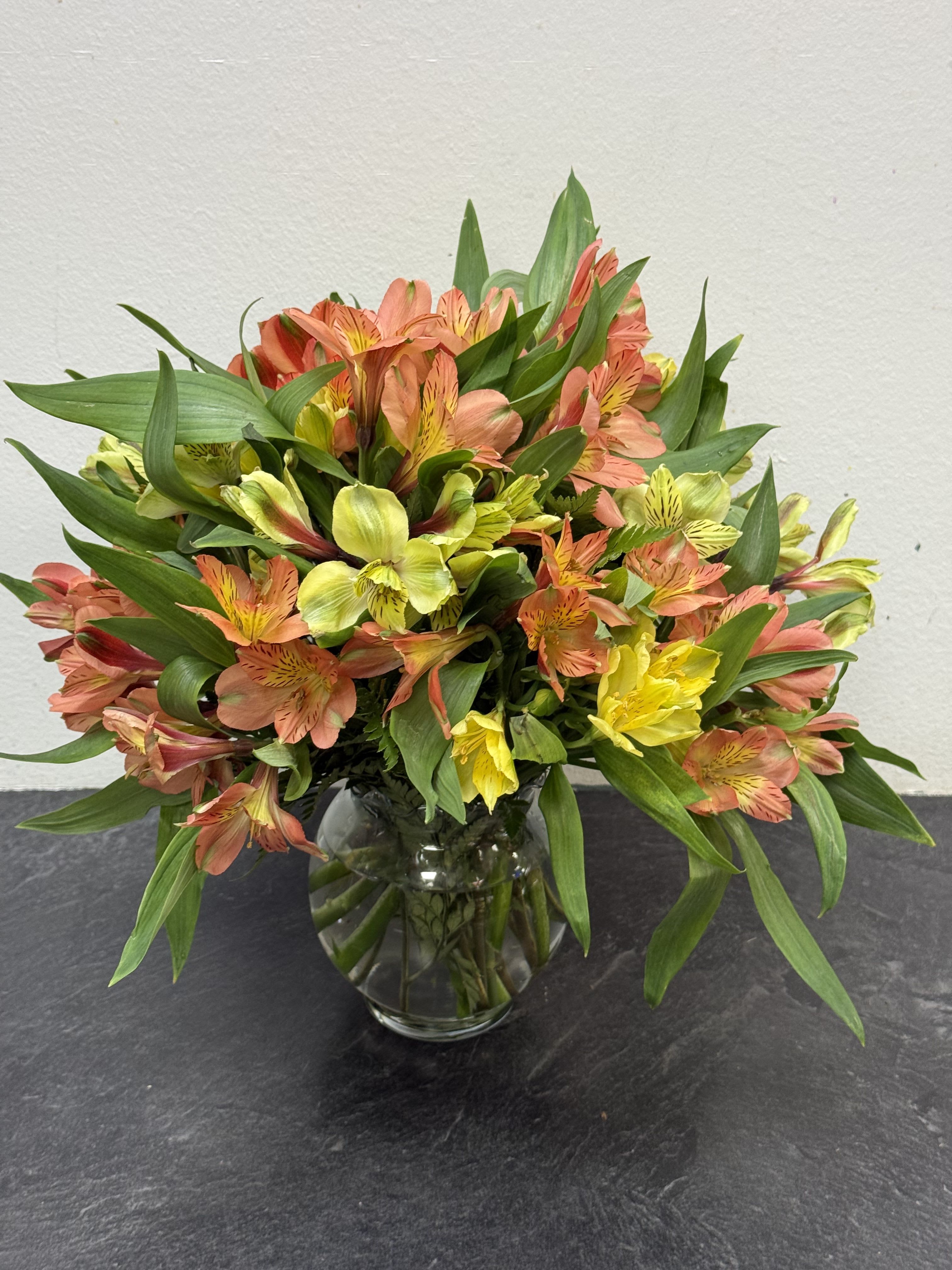 Mix alstroemeria  - A cheerful bouquet of orange and yellow alstroemeria blooms arranged in a classic clear glass vase. Their vibrant colors and long-lasting beauty bring the warmth of a sunset indoors, making this design a perfect gift for celebrations, gratitude, or simply brightening any day.