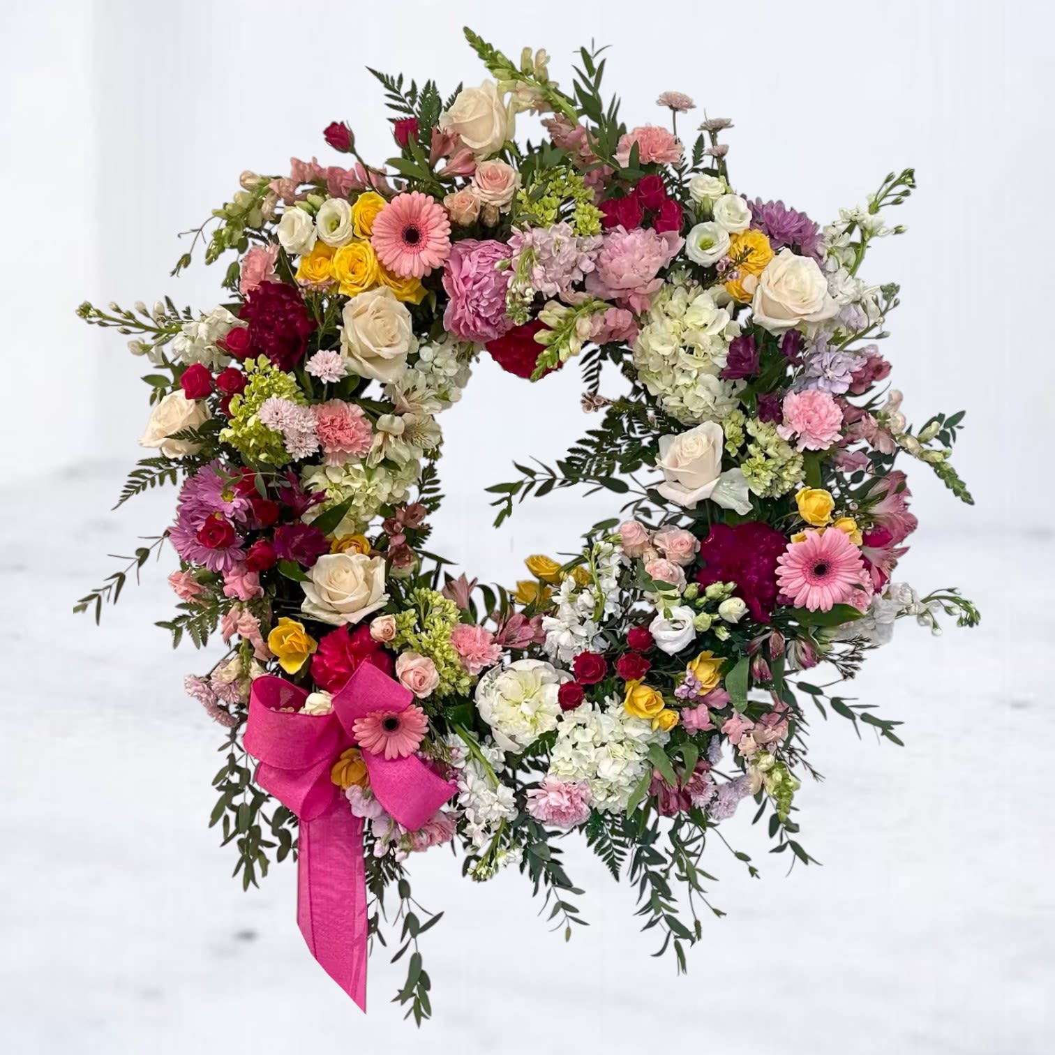 Shining Light Funeral Wreath Shining Light Funeral Wreath - Celebrate a life beautifully lived with the Shining Light Funeral Wreath, a radiant circle of blooms that speaks to joy, warmth, and cherished memories. Bursting with colorful roses, gerbera daisies, carnations, hydrangeas, snapdragons, lisianthus, and lush greenery, this heartwarming sympathy wreath blends soft pastels and bold hues with a bright pink bow for a heartfelt touch. Easels are included in the price of all wreath arrangements to ensure easy display at services. Designed to honor a loved one who brought color and kindness into every room, this standing wreath is perfect for funeral services, memorial ceremonies, or graveside tributes. Available for same-day funeral flower delivery in Houston, Magnolia, The Woodlands, Spring, Tomball, and surrounding areas.