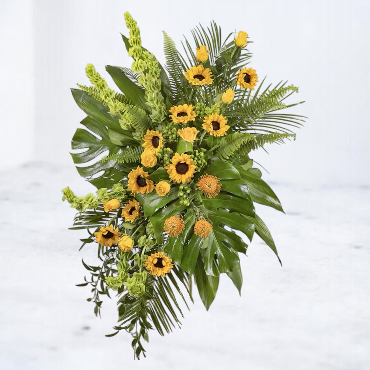 Propitious Horizon Standing Spray Propitious Horizon Standing Spray - Celebrate a life full of warmth and joy with the Propitious Horizon Standing Spray, a stunning standing spray that radiates light and love. Featuring vibrant sunflowers, golden roses, and exotic tropical greens, this arrangement is a perfect blend of elegance and brightness. Accented with Bells of Ireland and lush monstera leaves, it delivers a heartfelt message of remembrance while offering a sense of hope and renewal. Ideal for honoring a cherished loved one, this tribute is a beautiful addition to funeral or memorial services, reflecting a life that brought sunshine to others. Easels are included with all standing sprays for effortless display at services.