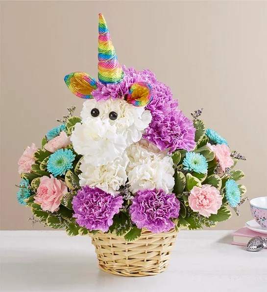 Enchanting Unicorn Enchanting Unicorn - Enchanting Unicorn™ — Magical Floral Gift in Houston  Bring a sprinkle of magic to any celebration with our Enchanting Unicorn™ floral arrangement, a whimsical creation perfect for dreamers of all ages. Handcrafted with delicate white, purple, and pink blooms, this charming bouquet is designed in the shape of a unicorn, complete with glittery rainbow ears and a mythical horn that truly brings fantasy to life.  Featuring white and lavender carnations, white button poms, and purple limonium accented with lush greenery, this 3D arrangement stands approximately 11" tall and 11" wide, nestled in a lined wicker pet basket. Expertly designed by local artisans, the Enchanting Unicorn™ makes a unique gift for birthdays, special occasions, or to brighten someone’s day in Houston with free same-day delivery.  Disclaimer: Our Puppy Love and Purrfection designs are exclusive to Floral Concepts and available only for delivery within our local Houston area.  Key Features:  Unique unicorn-shaped floral arrangement with white, lavender, and pink blooms  Glittery rainbow ears and horn for a magical touch  Includes white & lavender carnations, button poms, purple limonium, and assorted greenery  Measures approx. 11"H x 11"W, in a lined wicker pet basket  Handcrafted by Houston florists to ensure freshness and beauty  Celebrate imagination and wonder with the Enchanting Unicorn™, a perfect floral gift for kids, unicorn lovers, and anyone who appreciates a bit of enchantment.