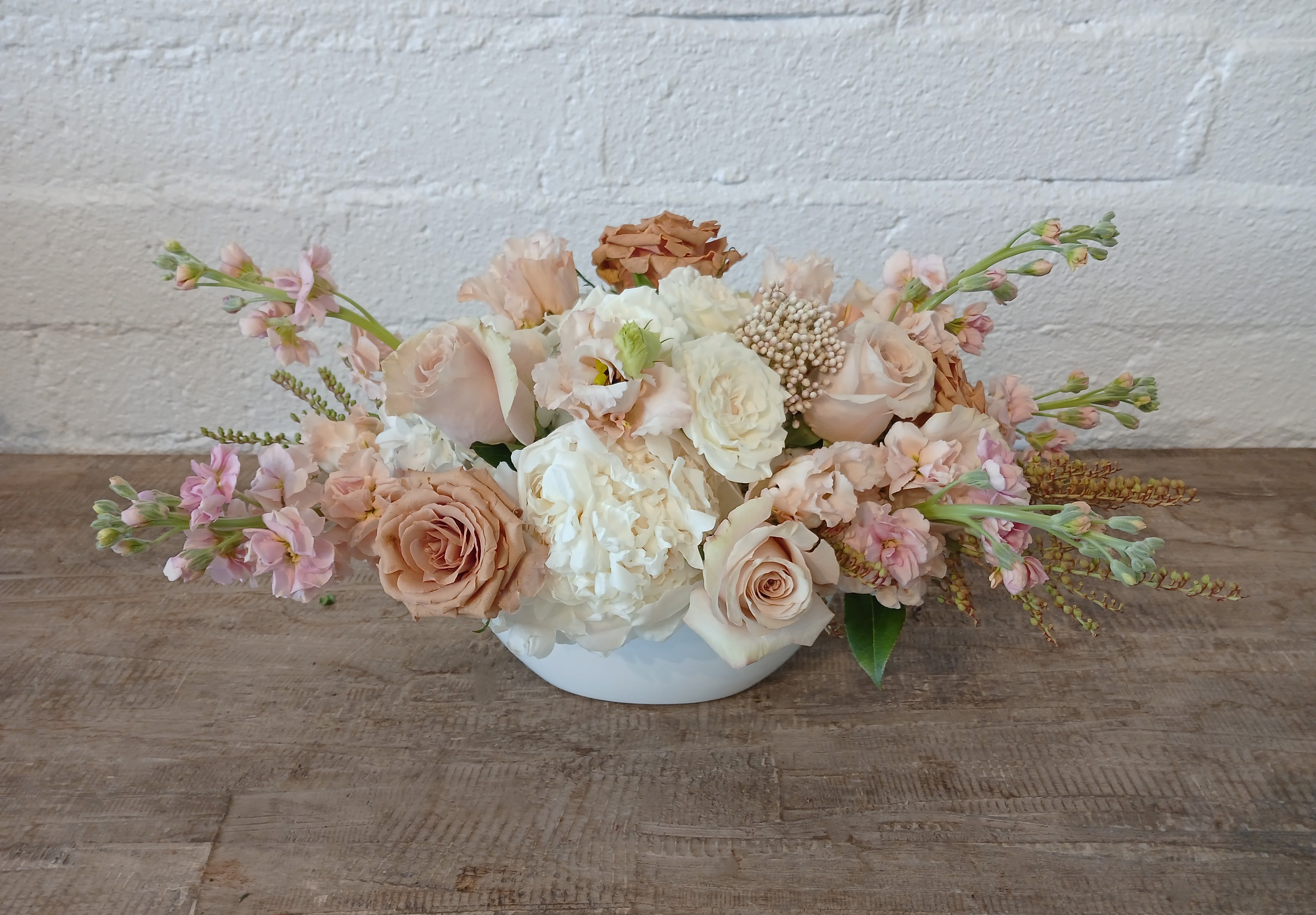 Soft Embrace - Soft Embrace is a serene and elegant floral arrangement that brings a gentle touch to any space. Featuring a lush mix of white, pastel pink, and nude flowers arranged in a clean, white ceramic vase. 