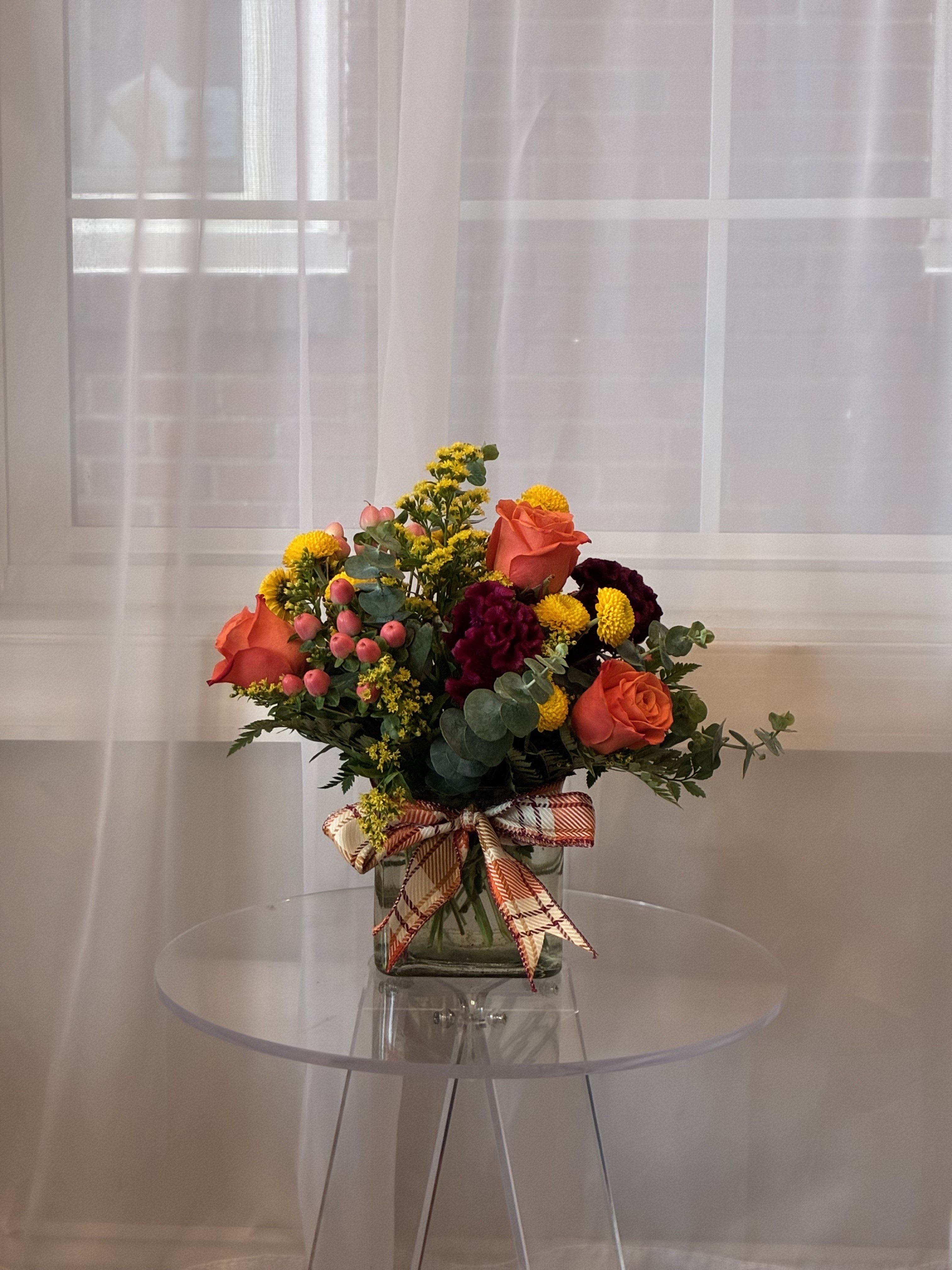 Golden Harmony - Celebrate life’s special moments with the radiant charm of our Golden Harmony arrangement.  This stunning bouquet features vibrant orange roses, wine colored celosia, cheerful yellow button poms, light pink hypericum berries, solidago, eucalyptus, and lush greenery.  All artfully arranged to create a warm and harmonious display. Perfect for brightening any room or expressing heartfelt sentiments, it’s tied together with a charming plaid ribbon for a touch of rustic elegance.