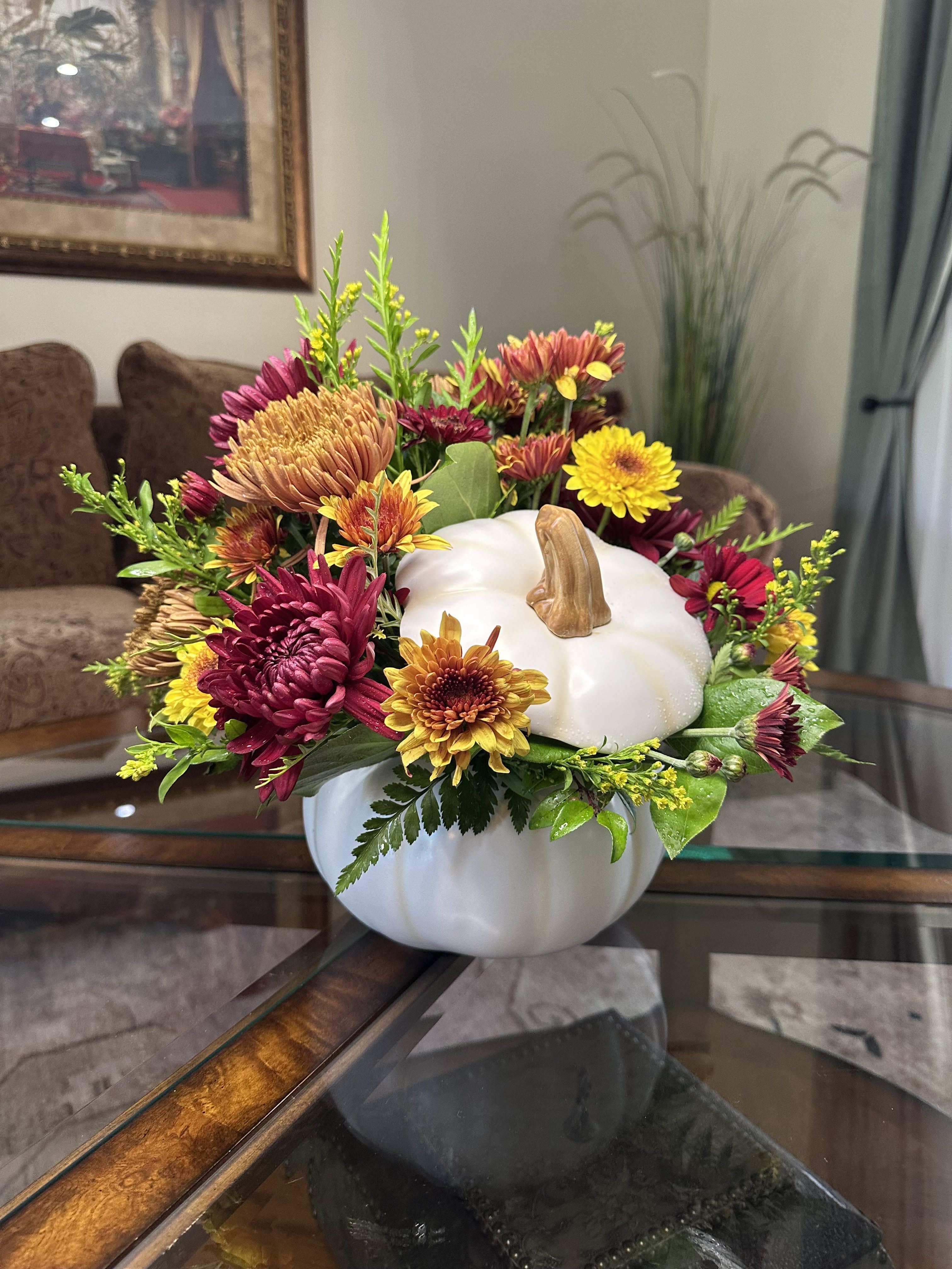 Pumpkin Spice Blooms Pumpkin Spice Blooms - Welcome the season with the cozy and inviting Pumpkin Spice Blooms. This eye-catching arrangement combines the rich colors of fall with a unique pumpkin-shaped vase. The beautiful blend of chrysanthemums in shades of crimson, gold, and amber creates a feeling of warmth and comfort, making it the perfect piece to add a touch of autumnal charm to your space.