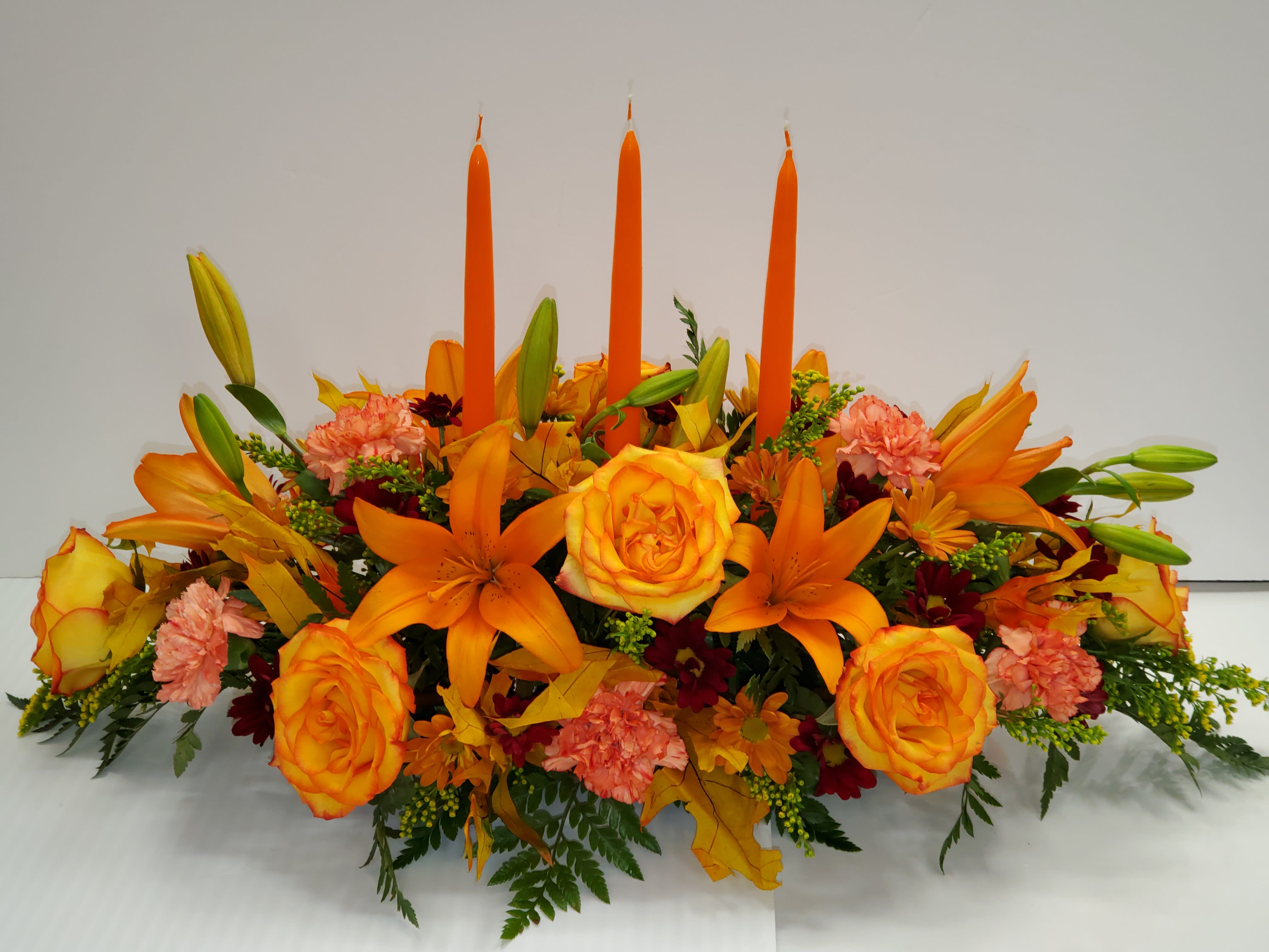 Grand Fall Centerpiece Grand Fall Centerpiece - 3 candles, 8 orange roses, 6 orange roses, 8 carnations, burgundy and orange fall daysis, 4 solidagos and fall leaf.