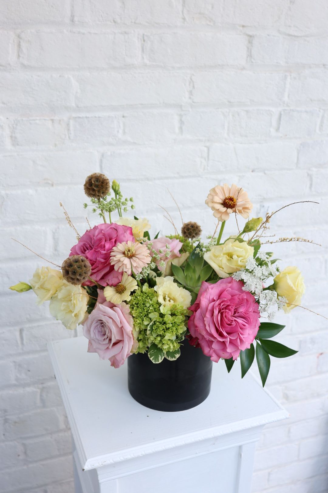Ellie - Pink and Green blooms with a succulent tucked in the middle, in a black ceramic cylinder vase with pops of dried elements 