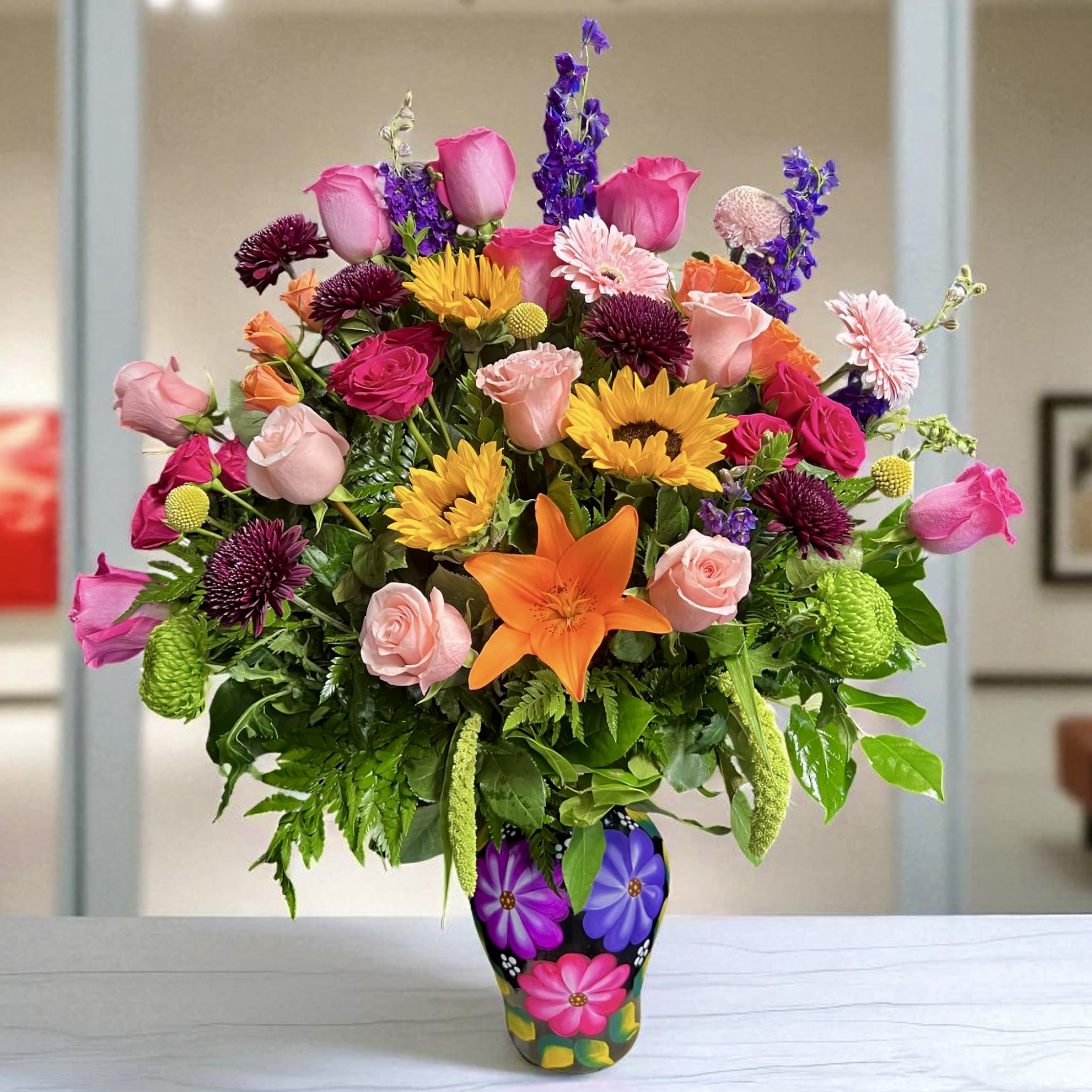 Fiesta Oaxaqueña - This vibrant arrangement is presented in a hand-painted ceramic vase from Oaxaca, Mexico, a region renowned for its rich artistic traditions. The vase is adorned with bright, colorful flowers painted by hand, reflecting the joyful and folkloric style of Oaxacan artisans. Each brushstroke celebrates Mexican craftsmanship, turning this container into a true work of art that perfectly complements the lively mix of fresh blooms above it.